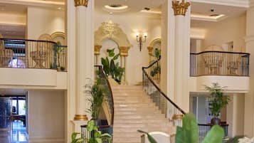 A grand lobby with a marble staircase, a mural on the ceiling, and a green sofa.