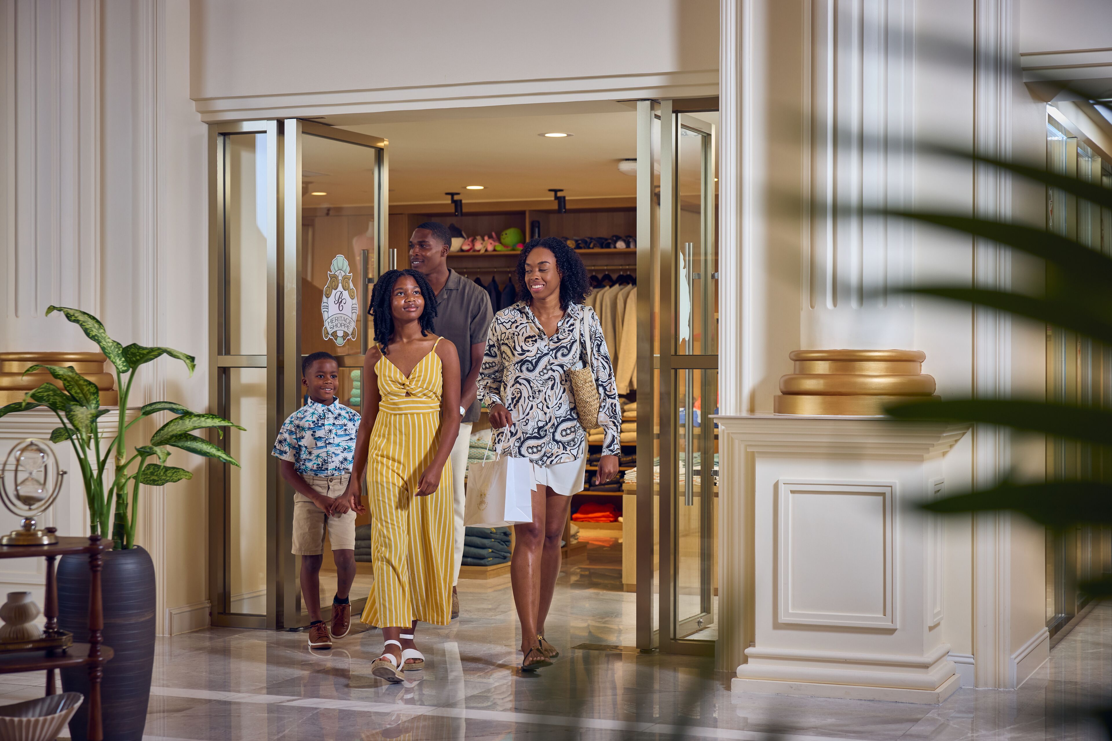 A family entering a hotel lobby with a modern design, featuring a reception desk and a large potted plant.