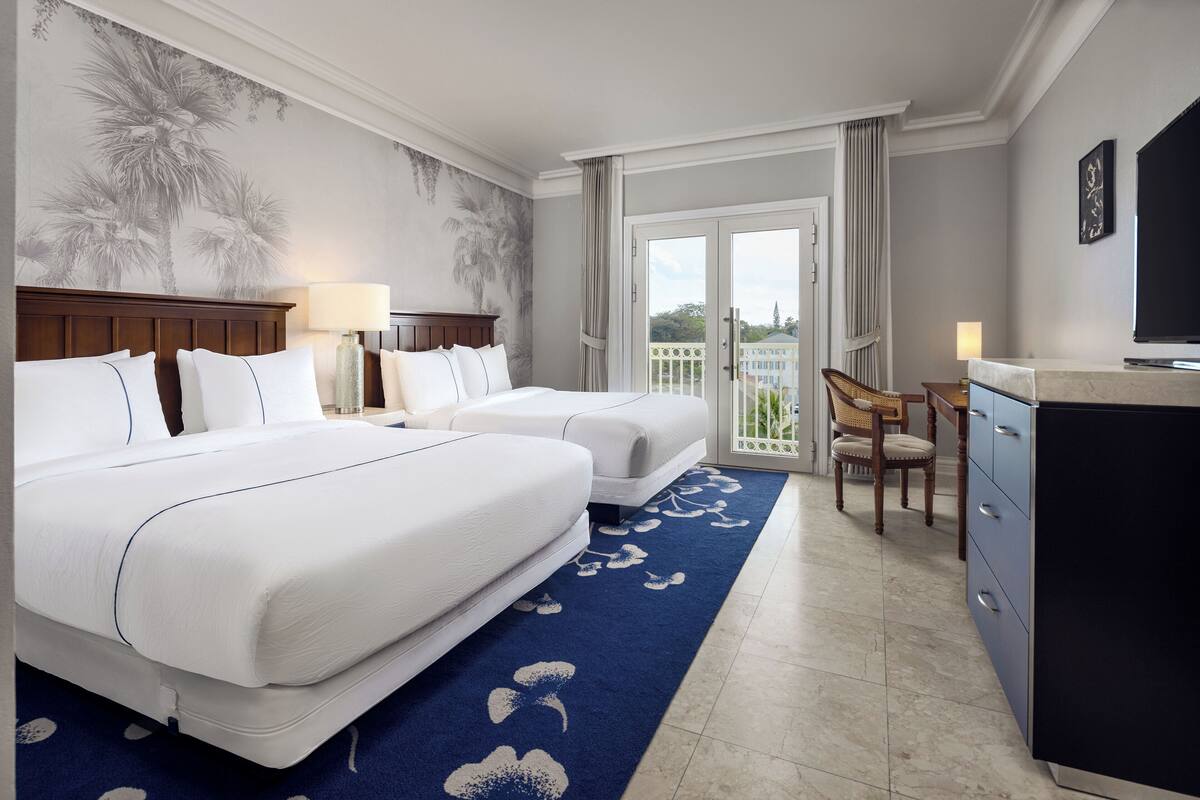 Quarto de hotel com duas camas, uma escrivaninha, televisão e varanda com vista.