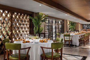 A dining area with round tables, green chairs, and a decorative lattice wall.