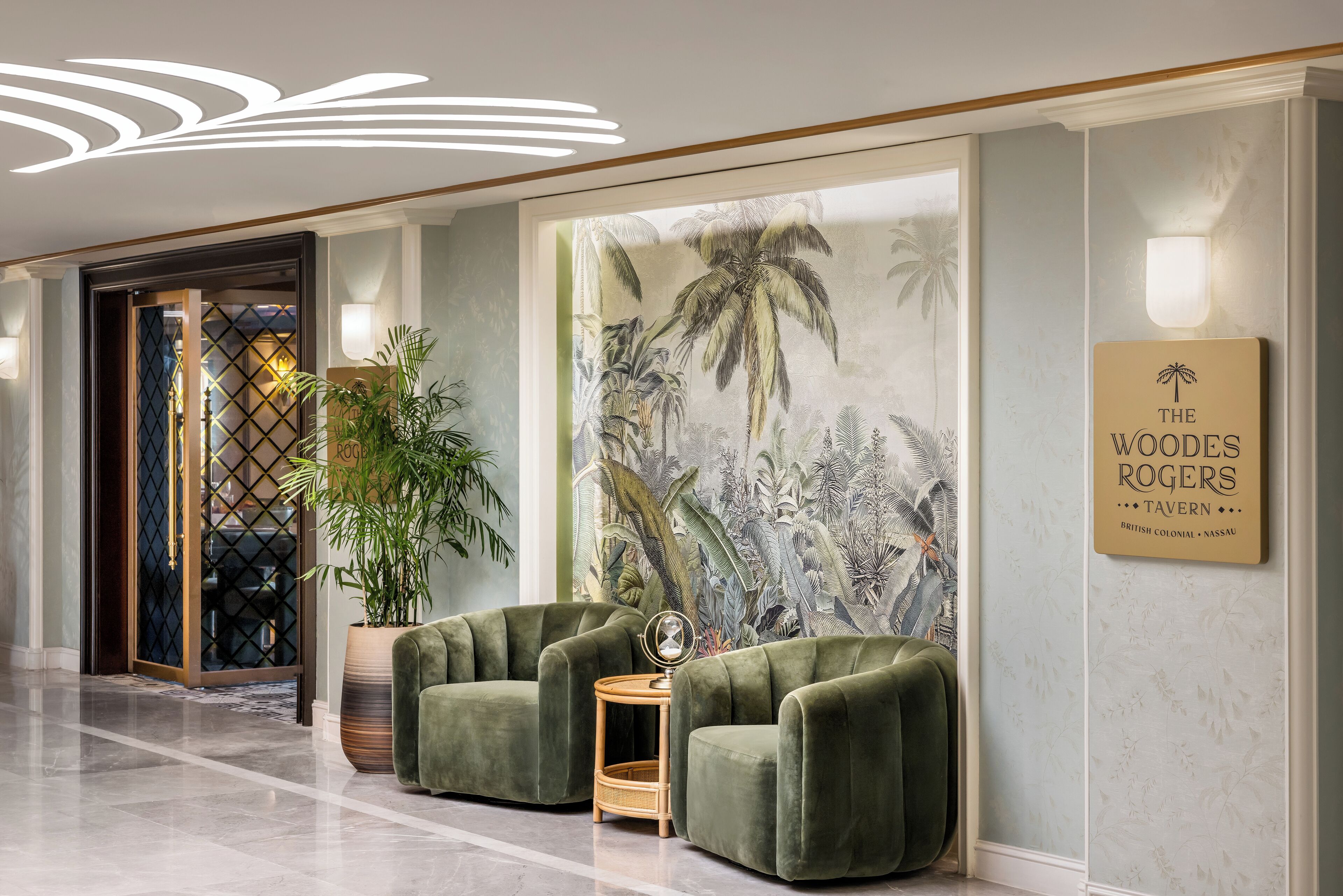 A lobby with a reception desk, two green armchairs, a large wall mural, and a sign for 'The Woodes Rogers Tavern'.