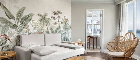A modern living room with a white sofa, a round wooden coffee table, and a large window with a view.