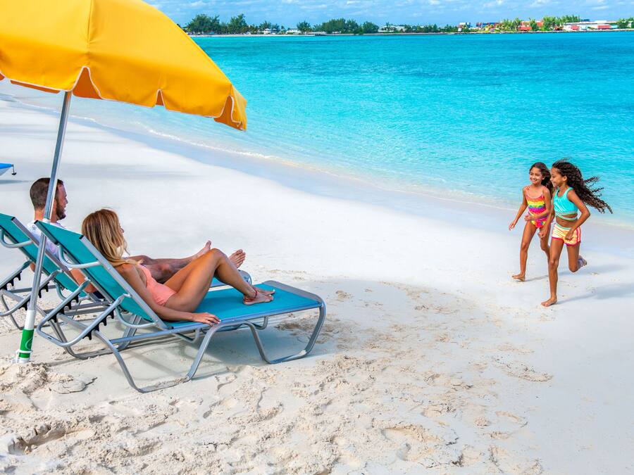 A beach with clear turquoise water, a sandy shore, and a yellow umbrella providing shade.