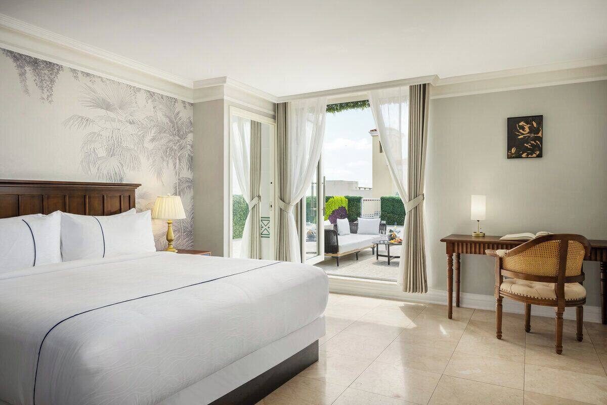 Quarto de hotel com cama grande, escrivaninha, cadeira e vista para a área externa.