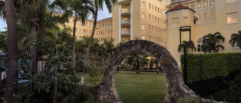 A hotel courtyard with a stone archway, palm trees, and a well-maintained lawn.