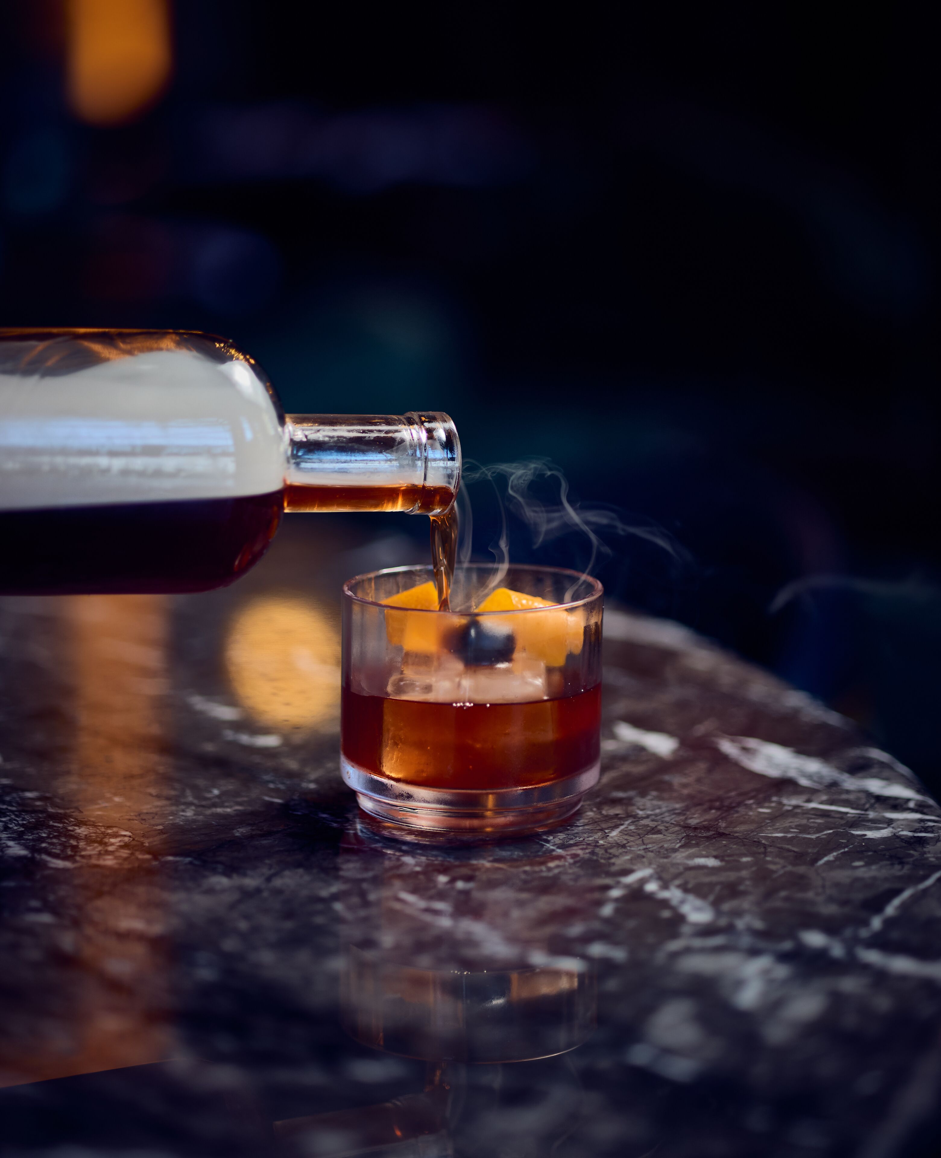 A clear glass of whiskey with ice cubes, being poured from a bottle.