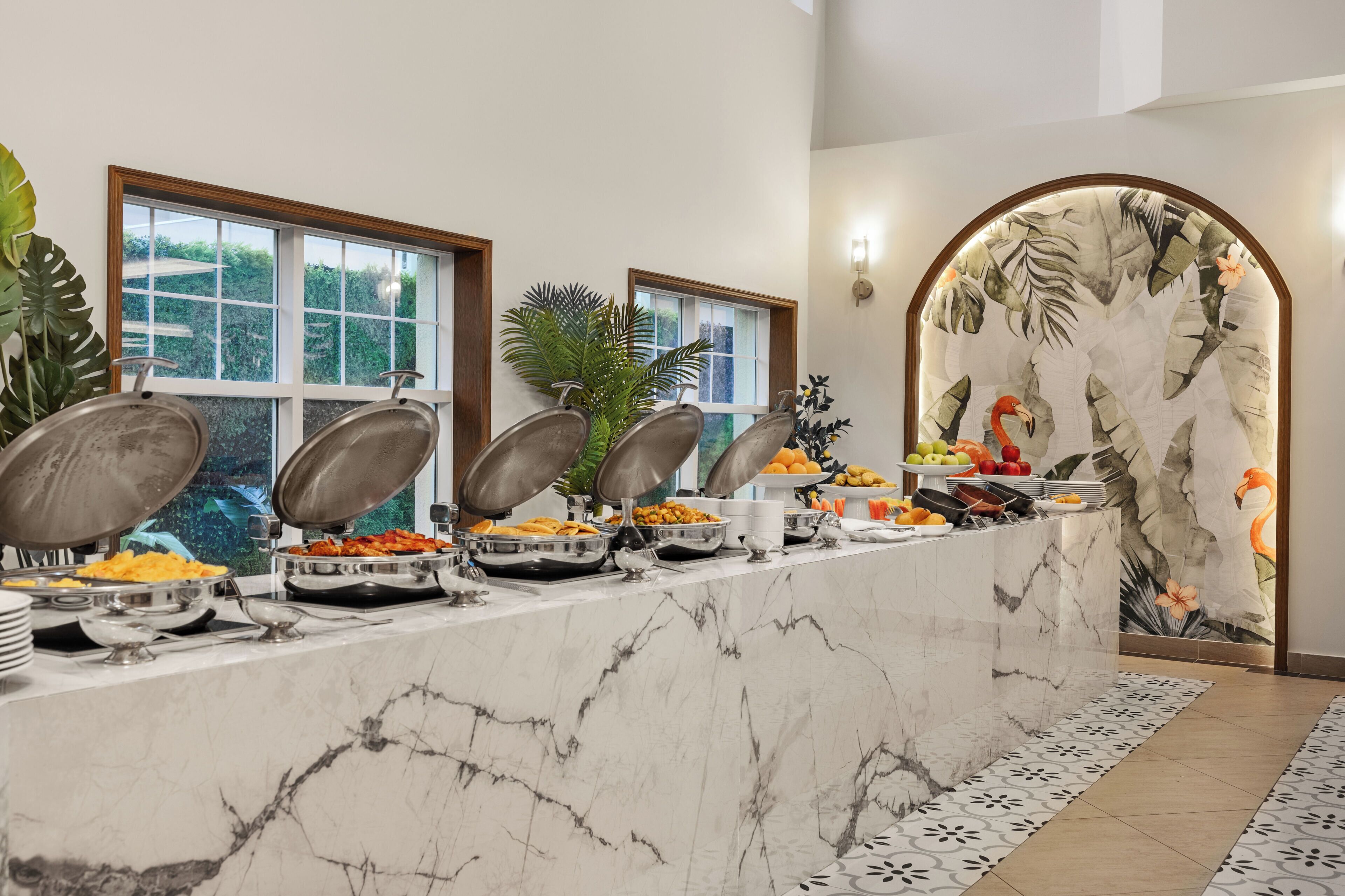 A buffet with various food items and a tropical-themed wall.