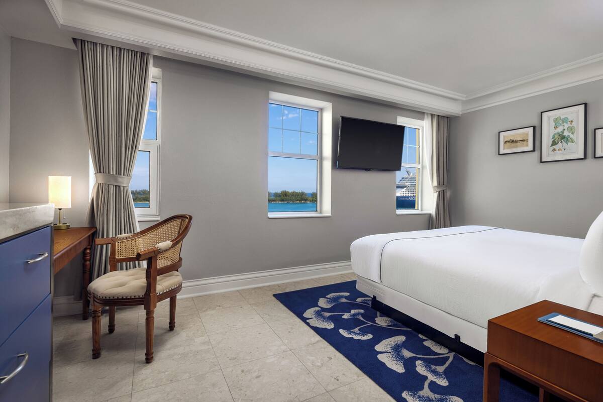 Quarto de hotel com cama, escrivaninha, cadeira, televisão e janela com vista.