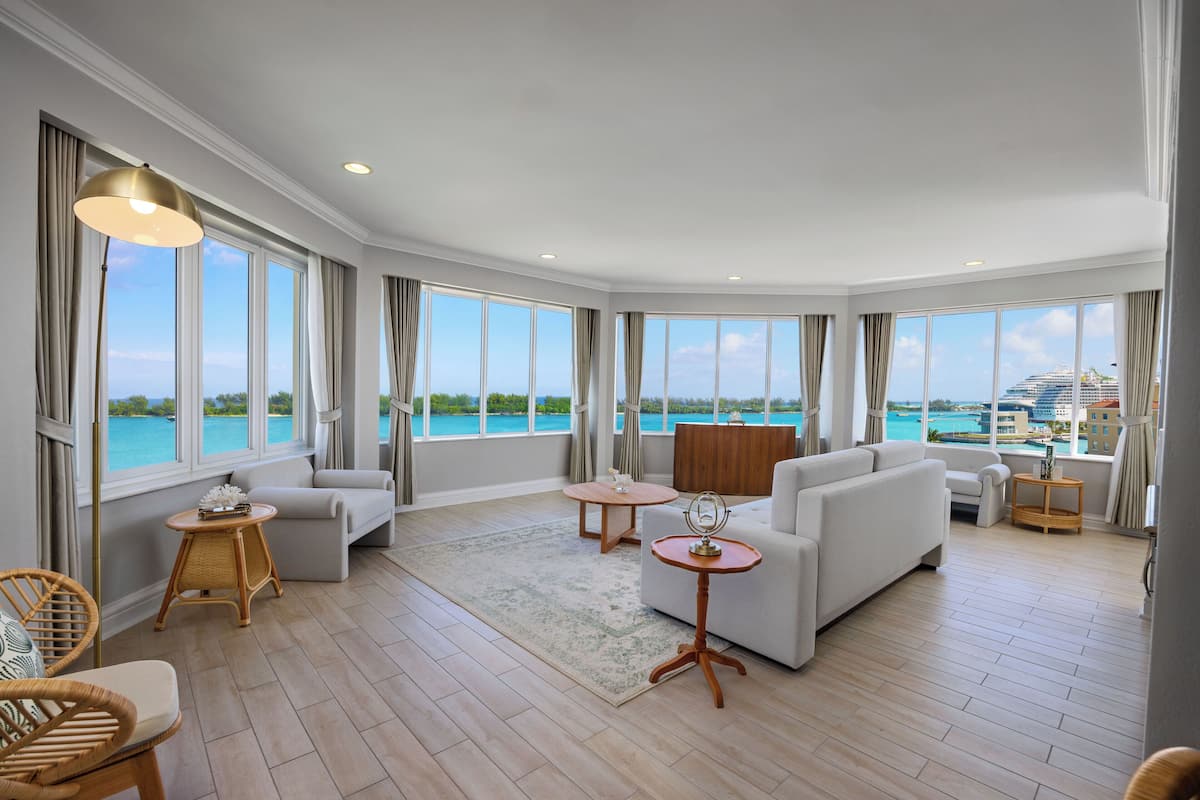 Uma sala de estar espaçosa com janelas grandes, um sofá, uma mesa de centro e vista para o mar.