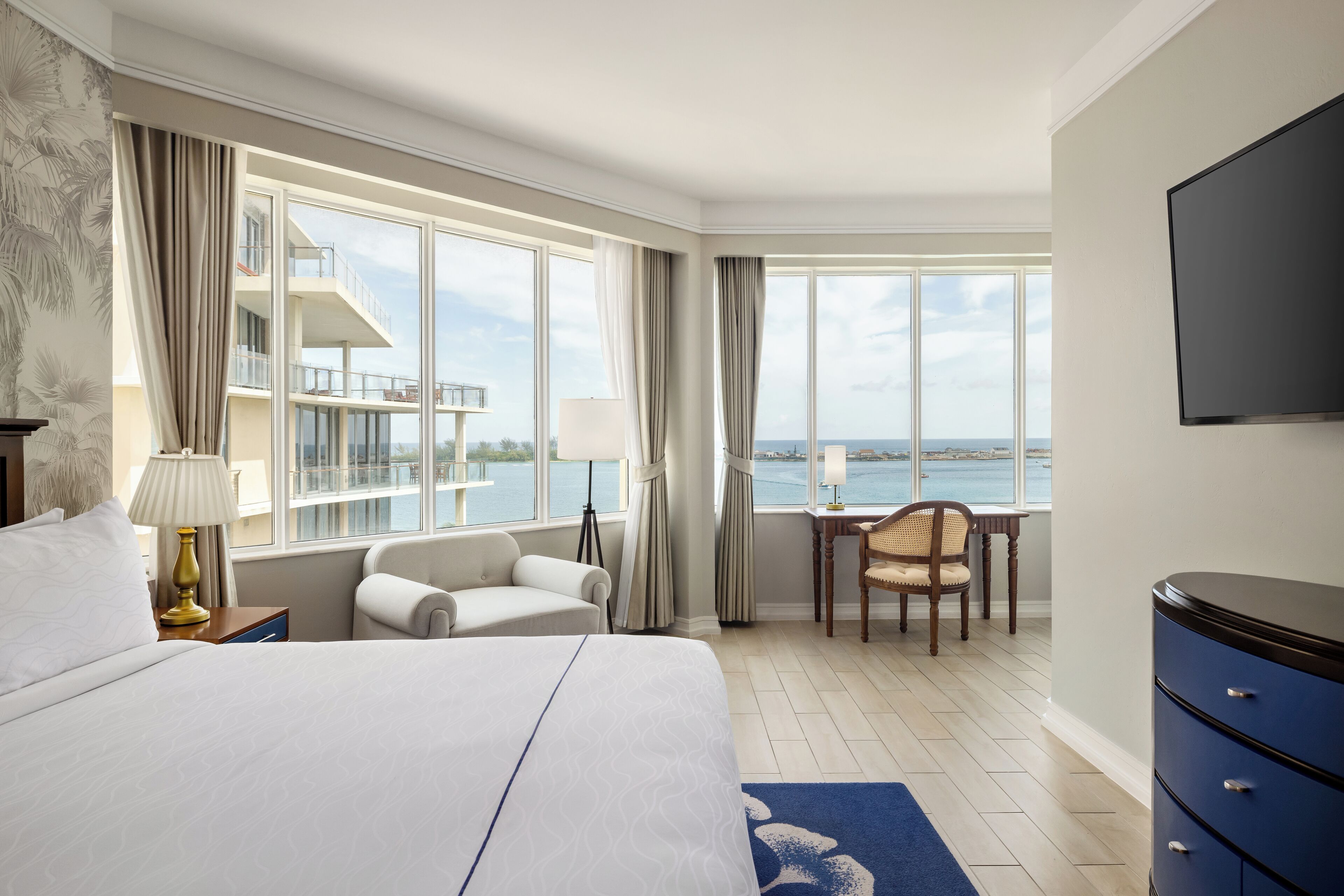 A hotel room with a large bed, a desk, a chair, and a view of the sea.