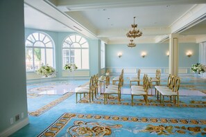 A spacious room with a blue carpet, white chairs, and large windows.
