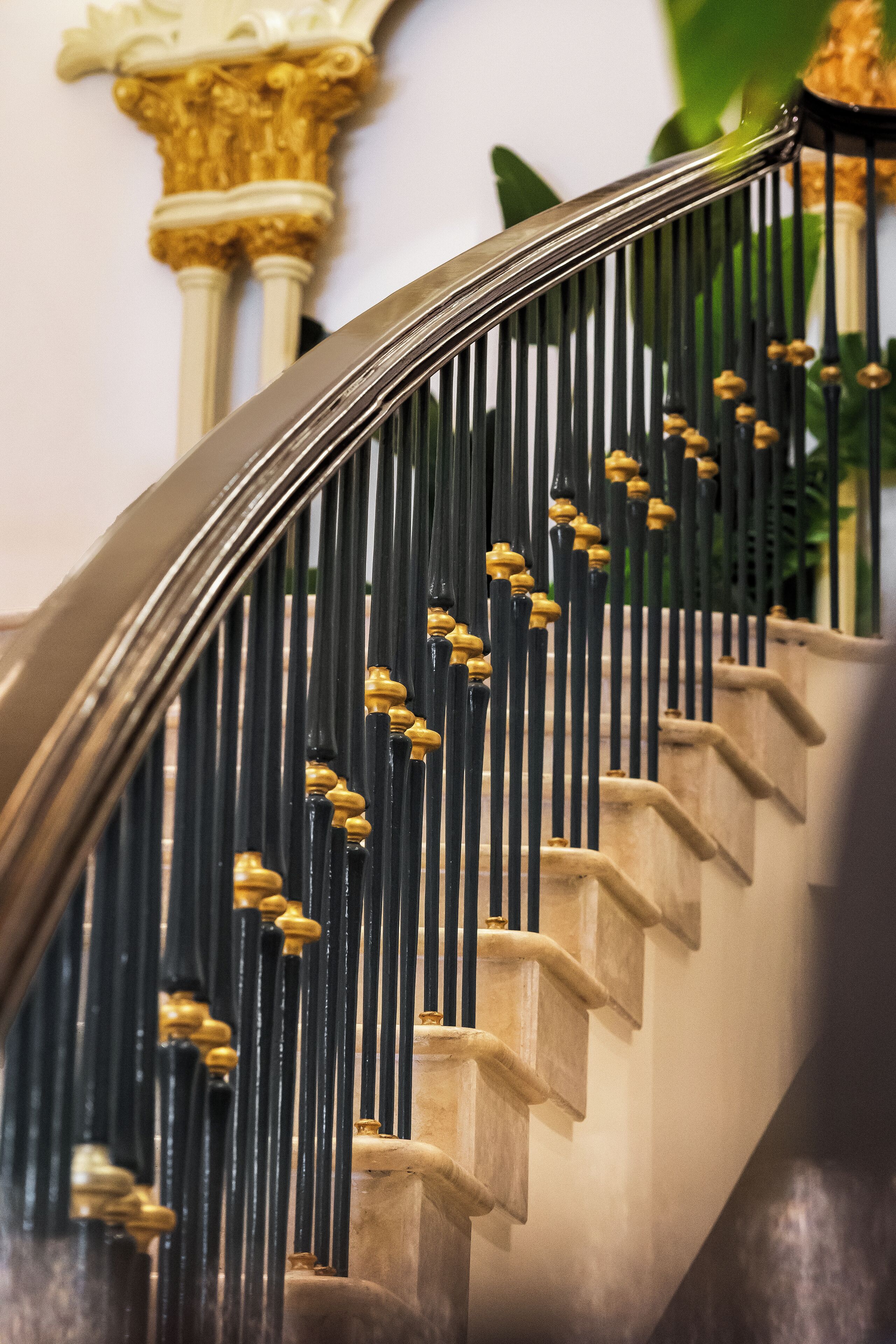 A staircase with black balusters and golden accents, leading to a landing with a decorative column.