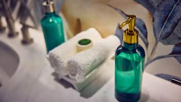 Une salle de bain avec un lavabo blanc, deux flacons de savon liquide, une serviette blanche et un distributeur de savon.