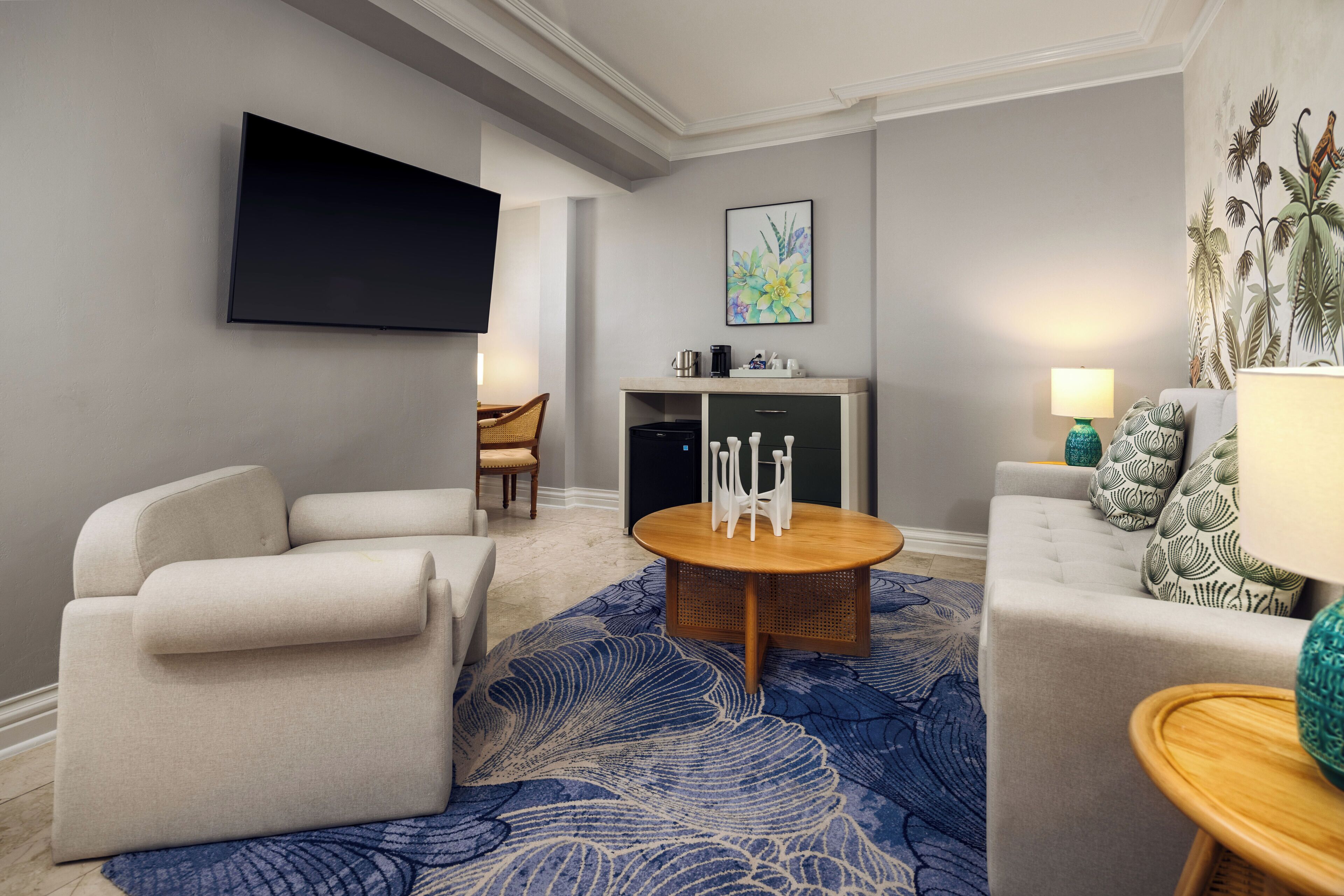 Una sala de estar moderna con una televisión de pantalla plana, un sofá, un sillón, una mesa de centro y una alfombra estampada.