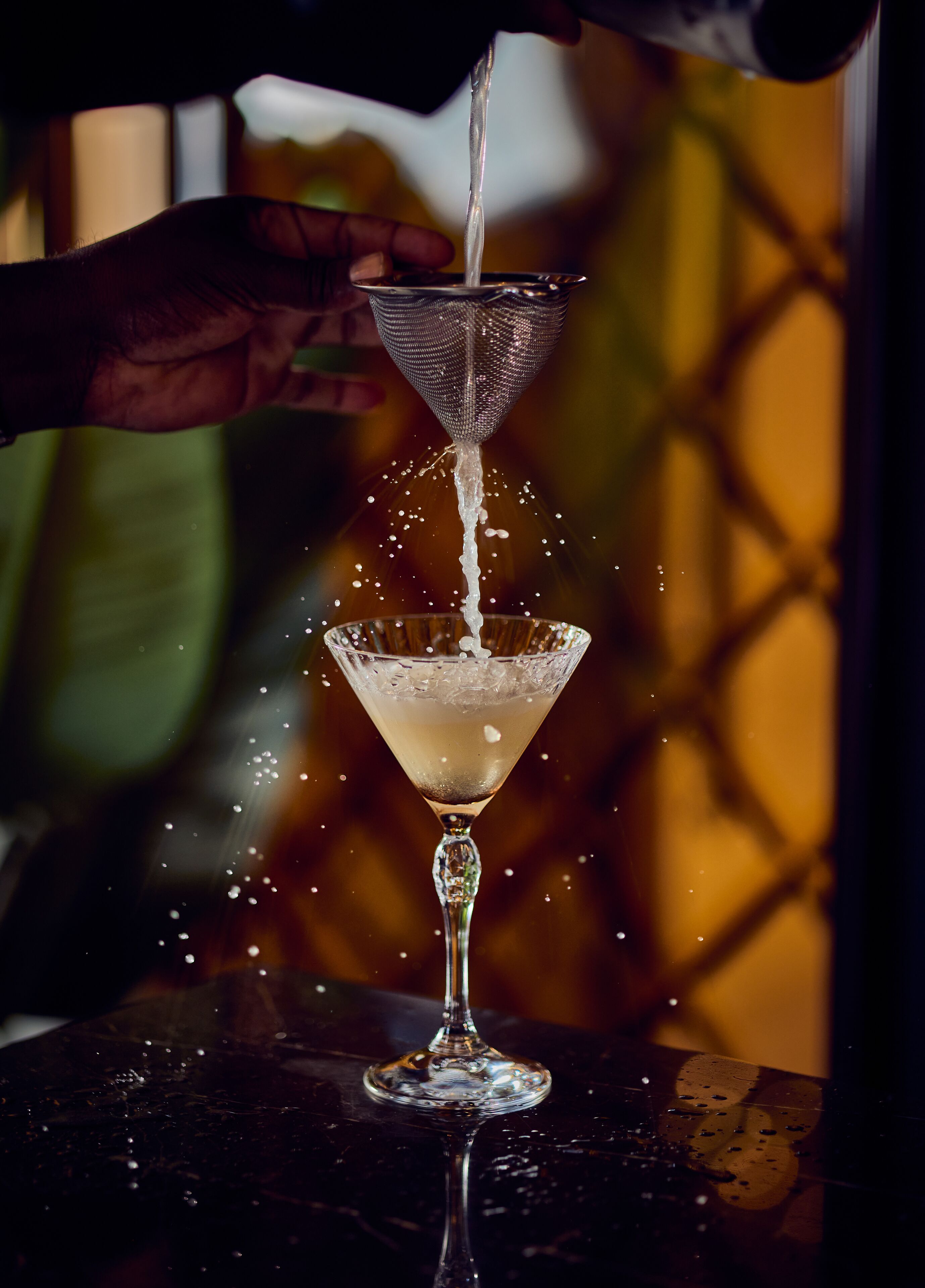 Una mano vertiendo un líquido en una copa de martini.