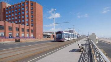Un tranvía sobre rieles, una acera para peatones y un edificio con varias ventanas.