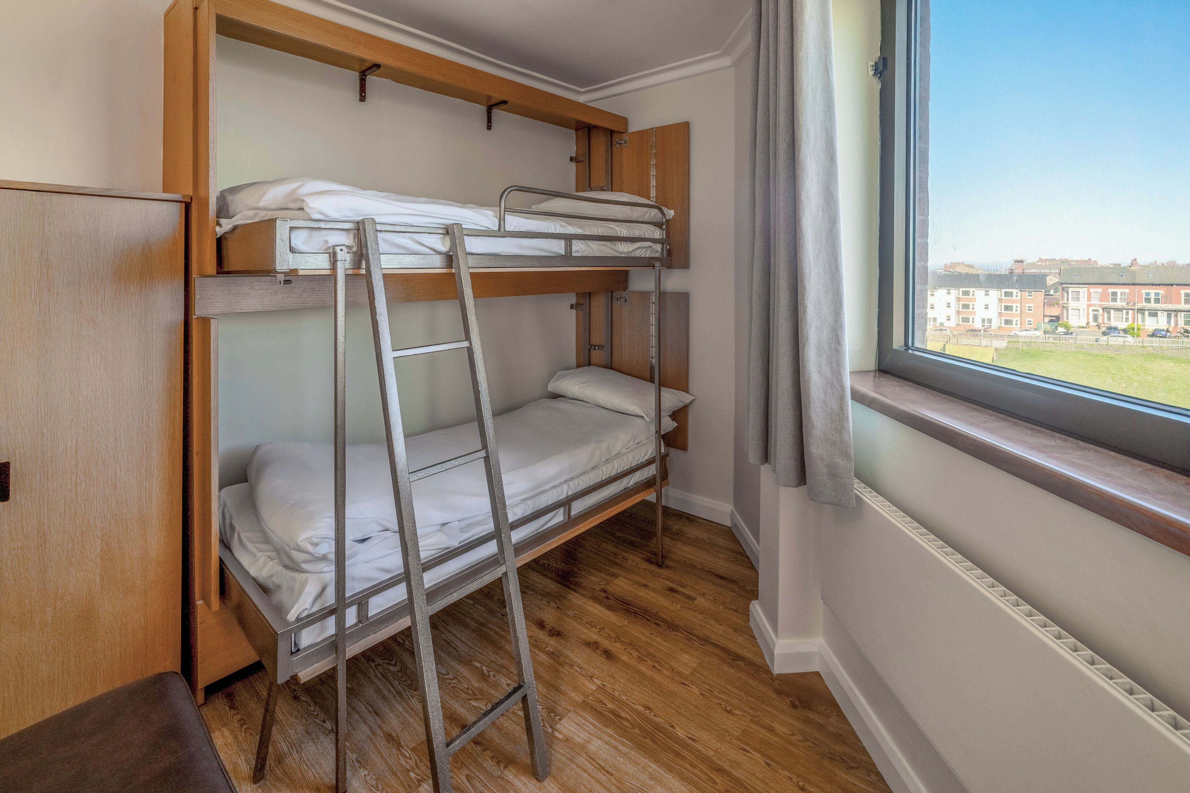 Habitación con literas, ventana, suelo de madera y radiador.