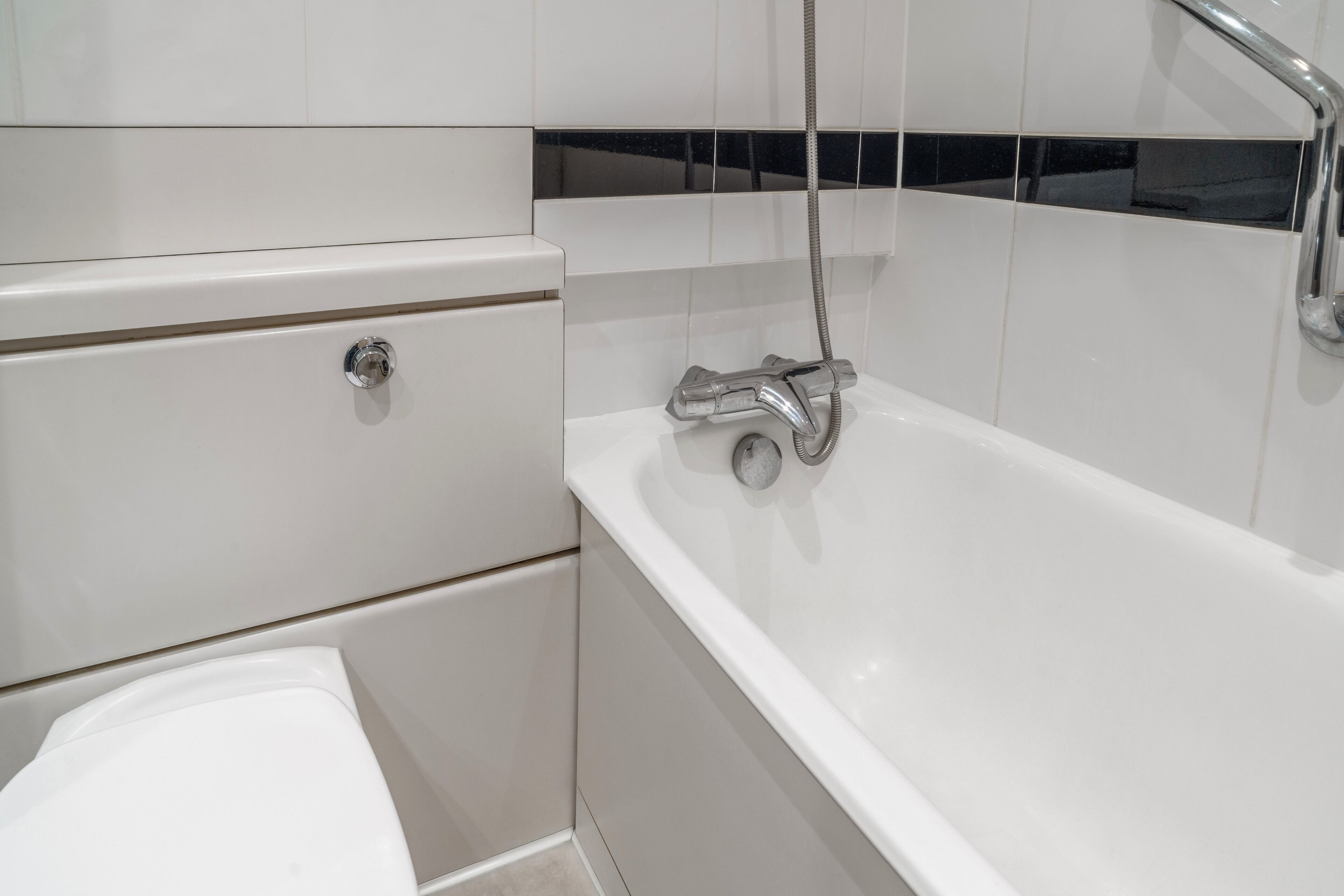 A bathroom with a white bathtub, a showerhead, and a toilet.
