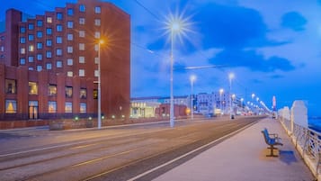A tram track with a bench on the right, a building with multiple windows on the left, and a clear sky.