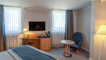A hotel room with a bed, a desk, a chair, a TV, and a lamp.