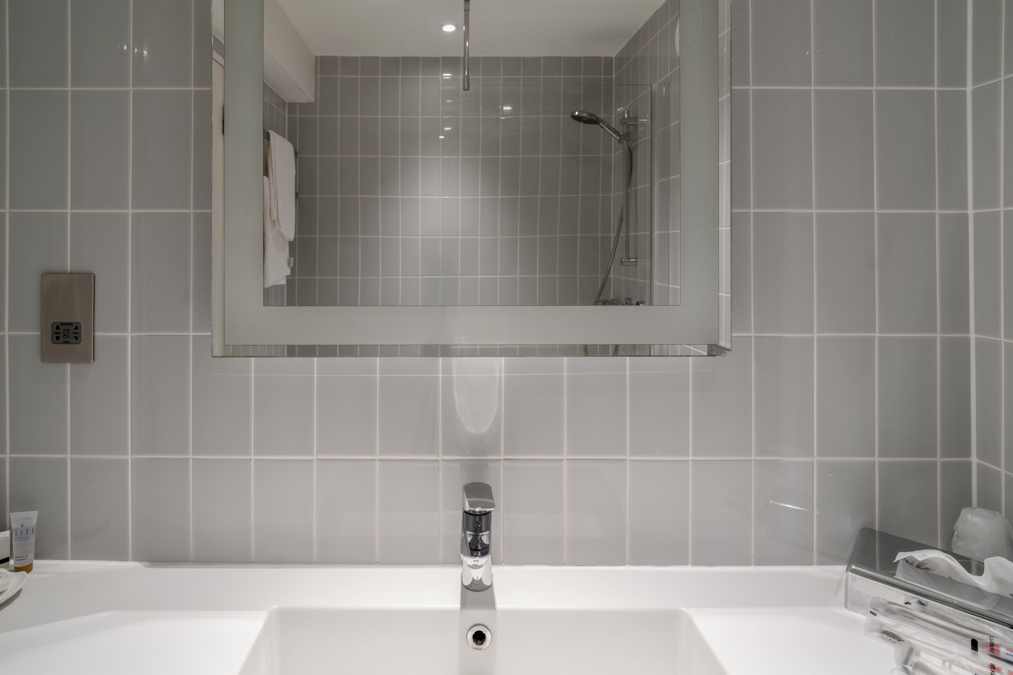 Baño con lavamanos blanco, espejo y ducha.