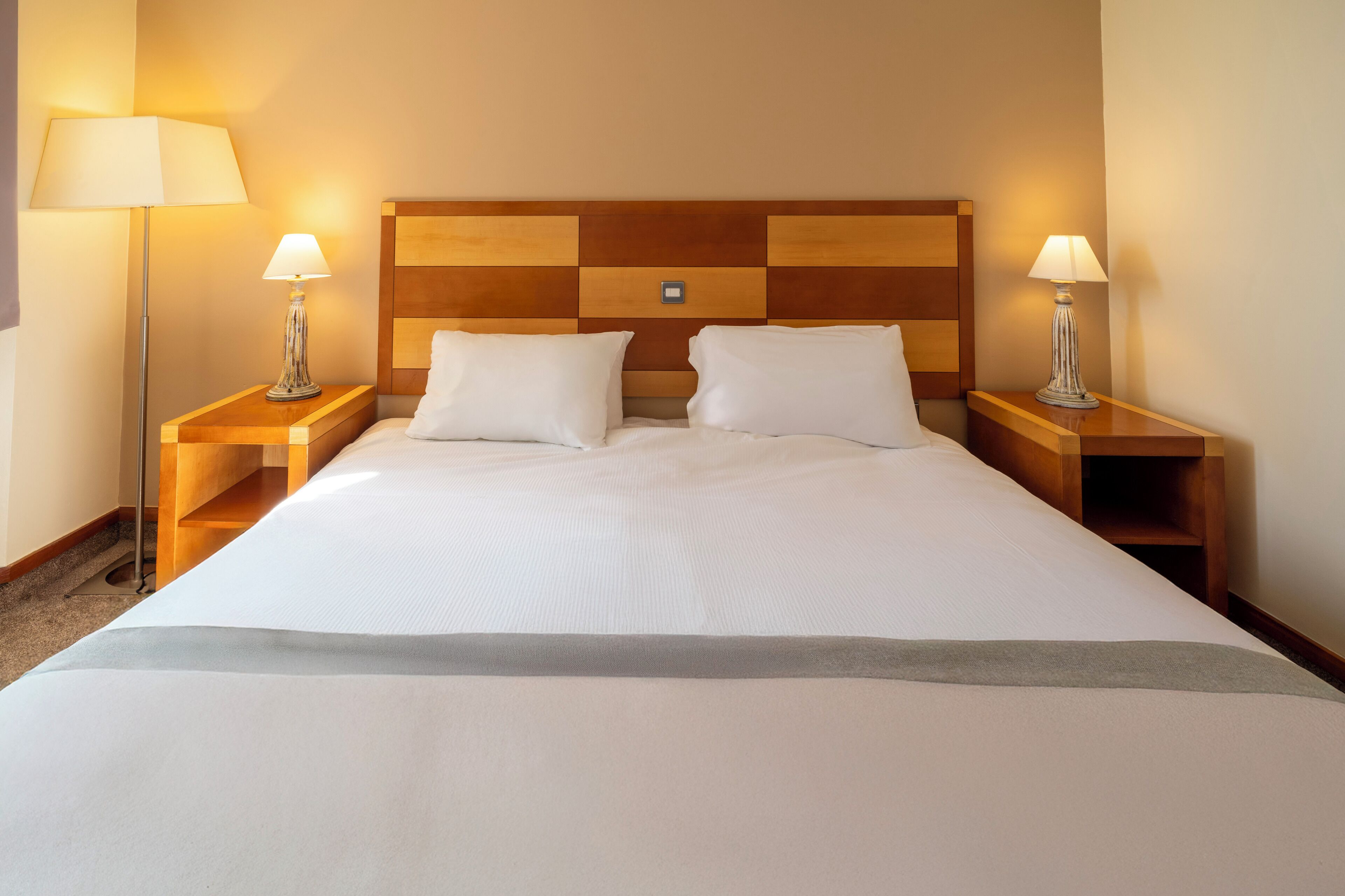 Une chambre d’hôtel avec un grand lit, deux tables de chevet avec des lampes, une tête de lit en bois et une petite table de nuit.