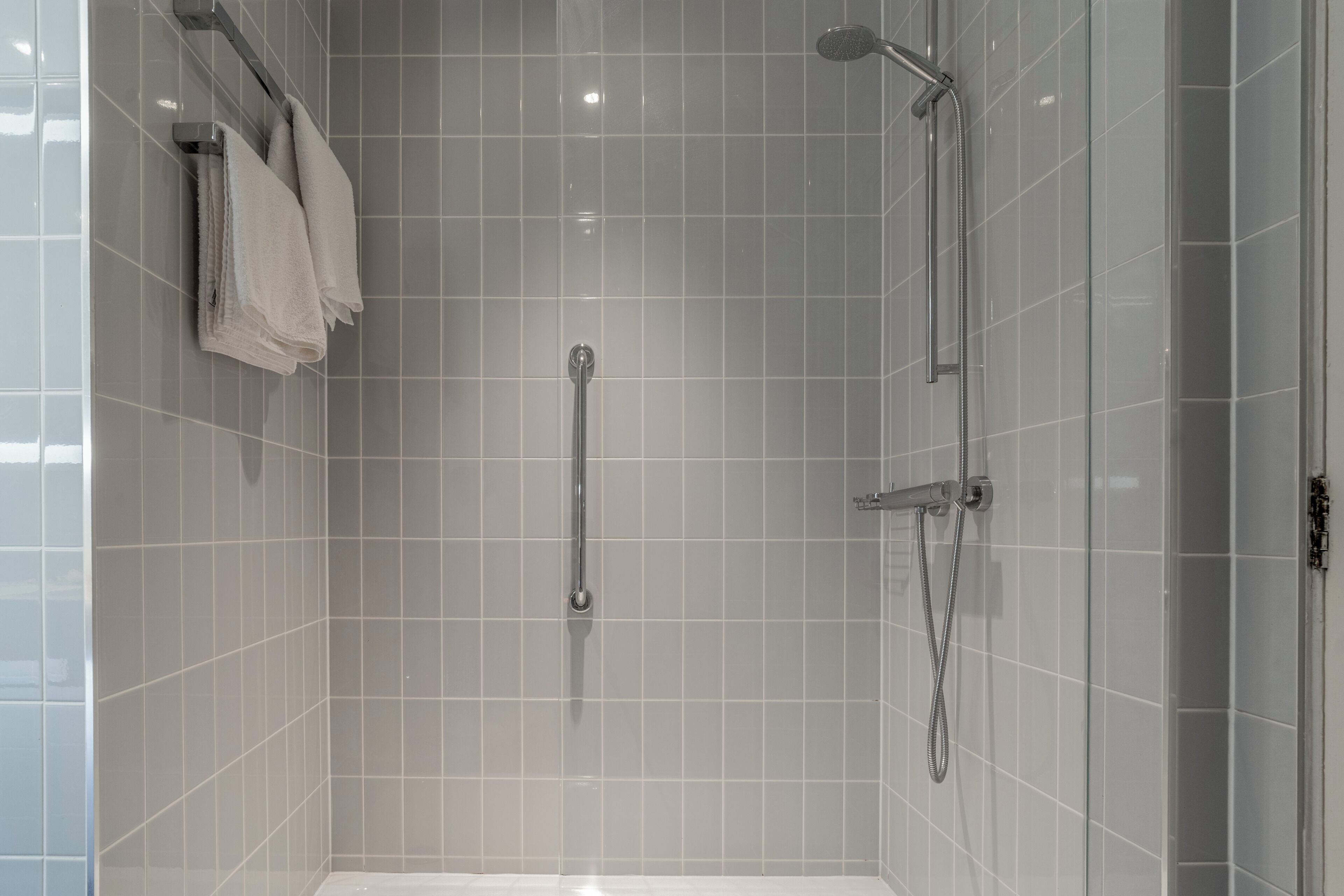A modern bathroom with a shower, a handrail, and a towel rack.