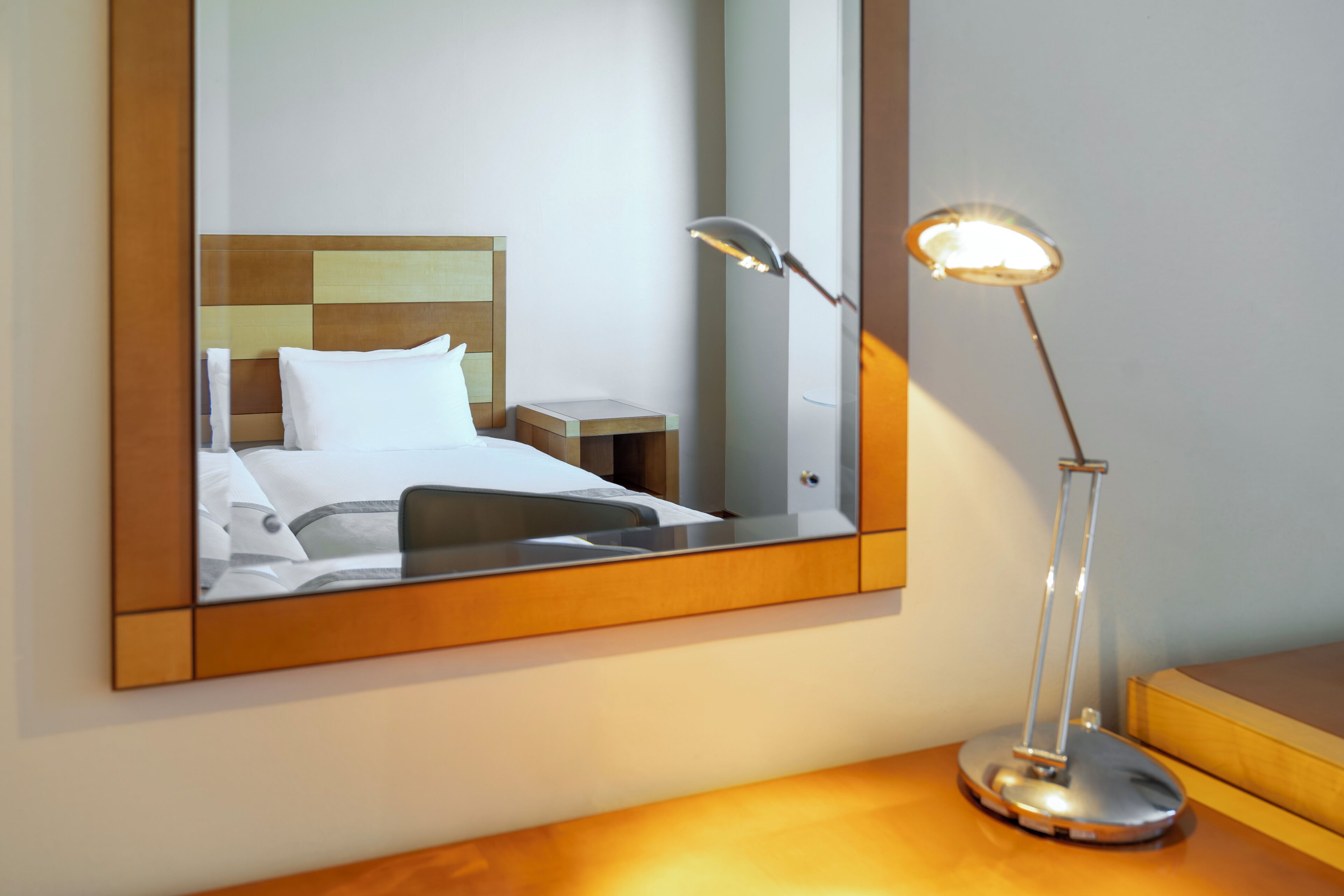 A hotel room with a bed, a nightstand, a lamp, and a mirror reflecting the room.