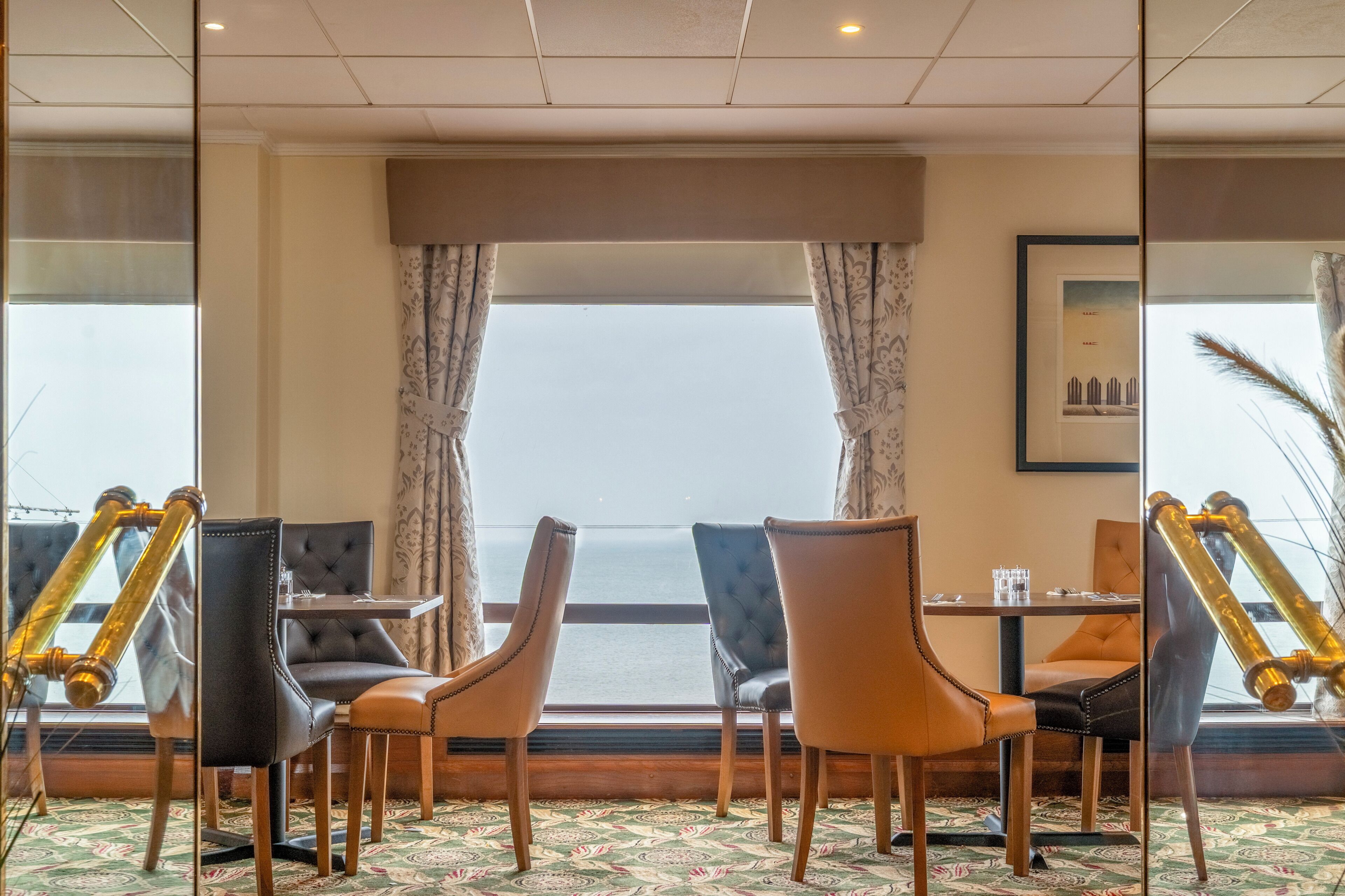 A room with a view of the sea, a table with chairs, and a large mirror.
