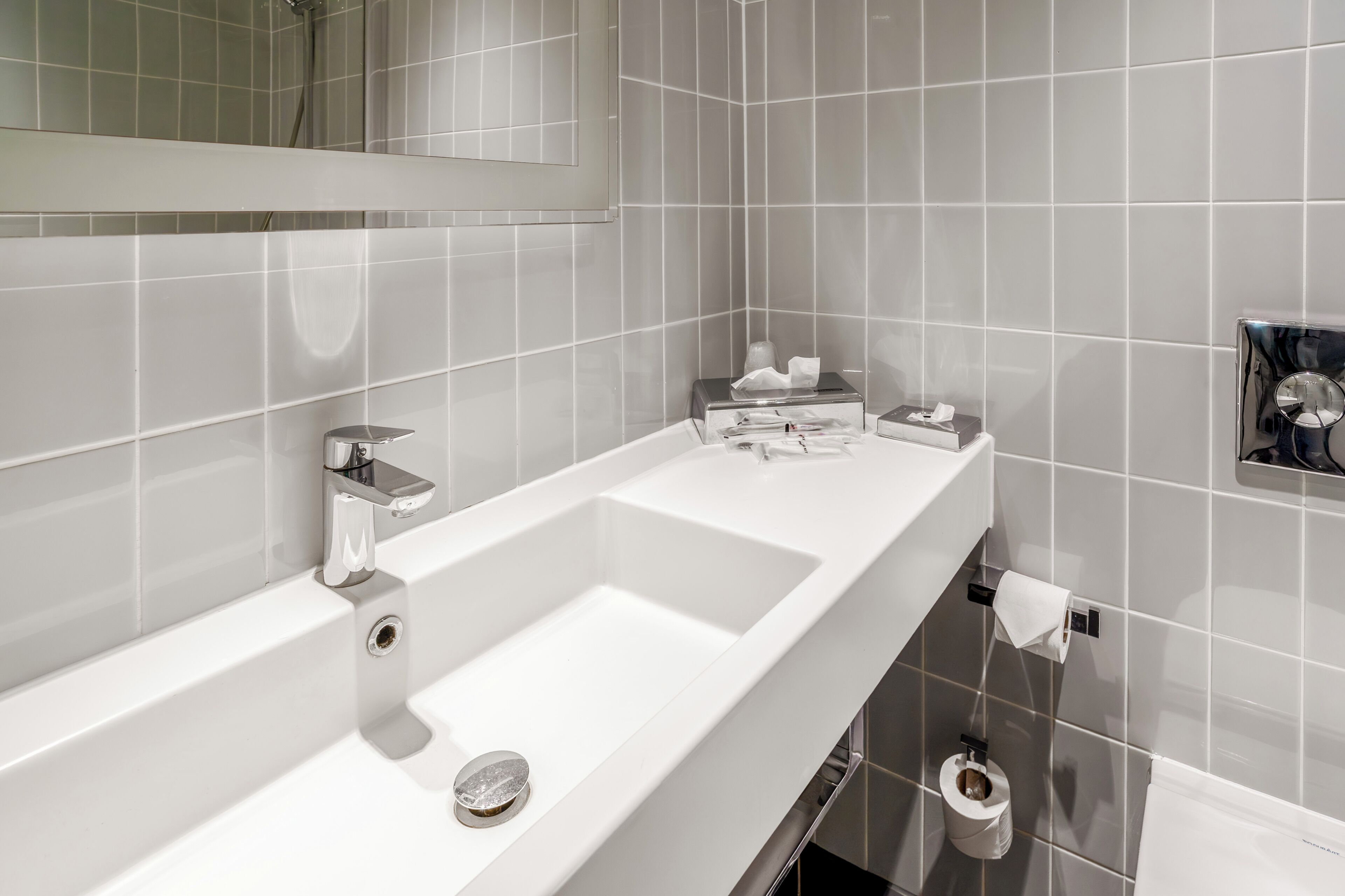 A modern bathroom with a large mirror, two sinks, and a toilet.