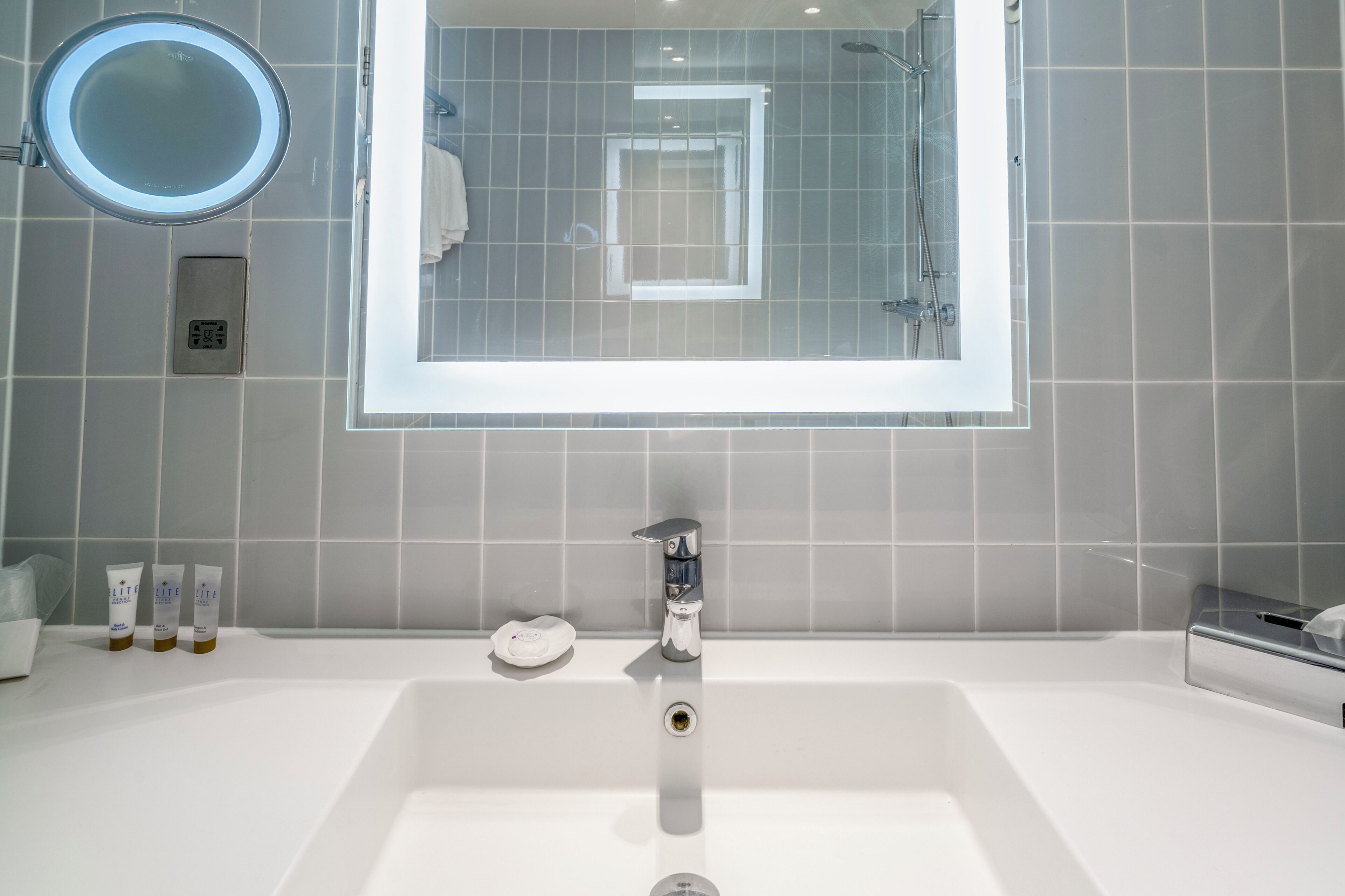 Ein modernes Badezimmer mit einem großen Spiegel, einer Duschkabine und einem weißen Waschbecken.