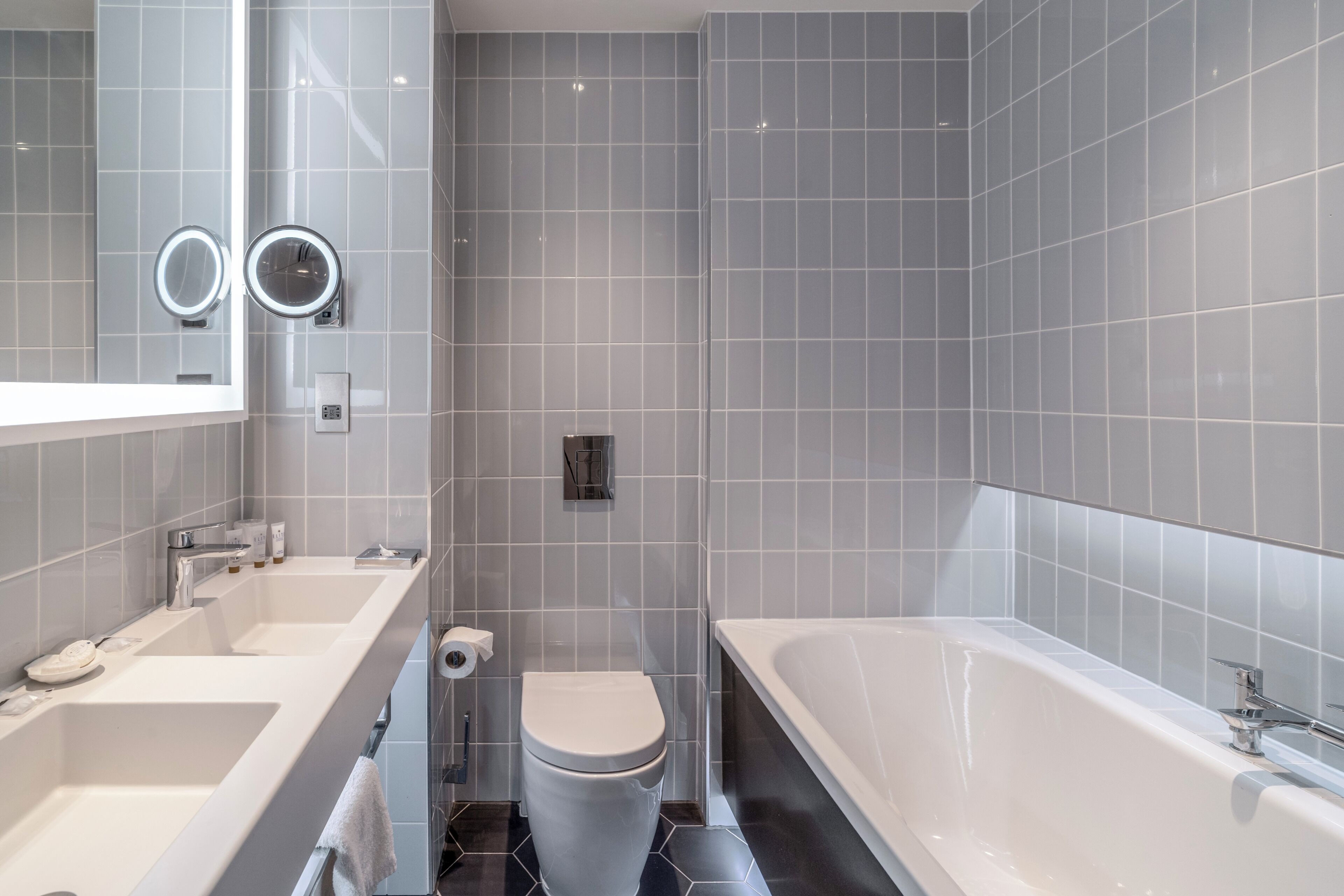 Un baño moderno con un espejo grande, dos lavamanos, un inodoro y una bañera.