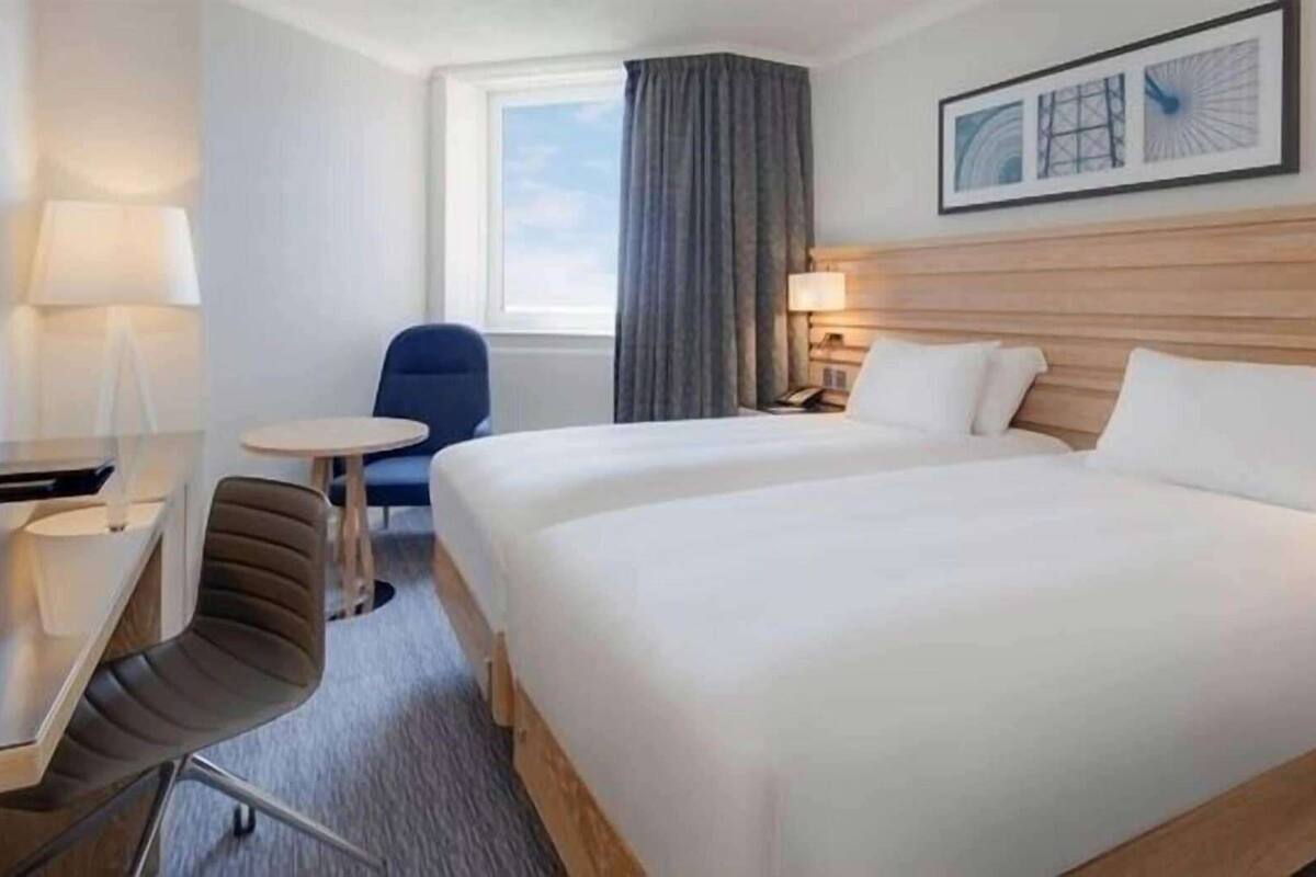 A hotel room with a large bed, a desk, a chair, a small table, and a window with curtains.