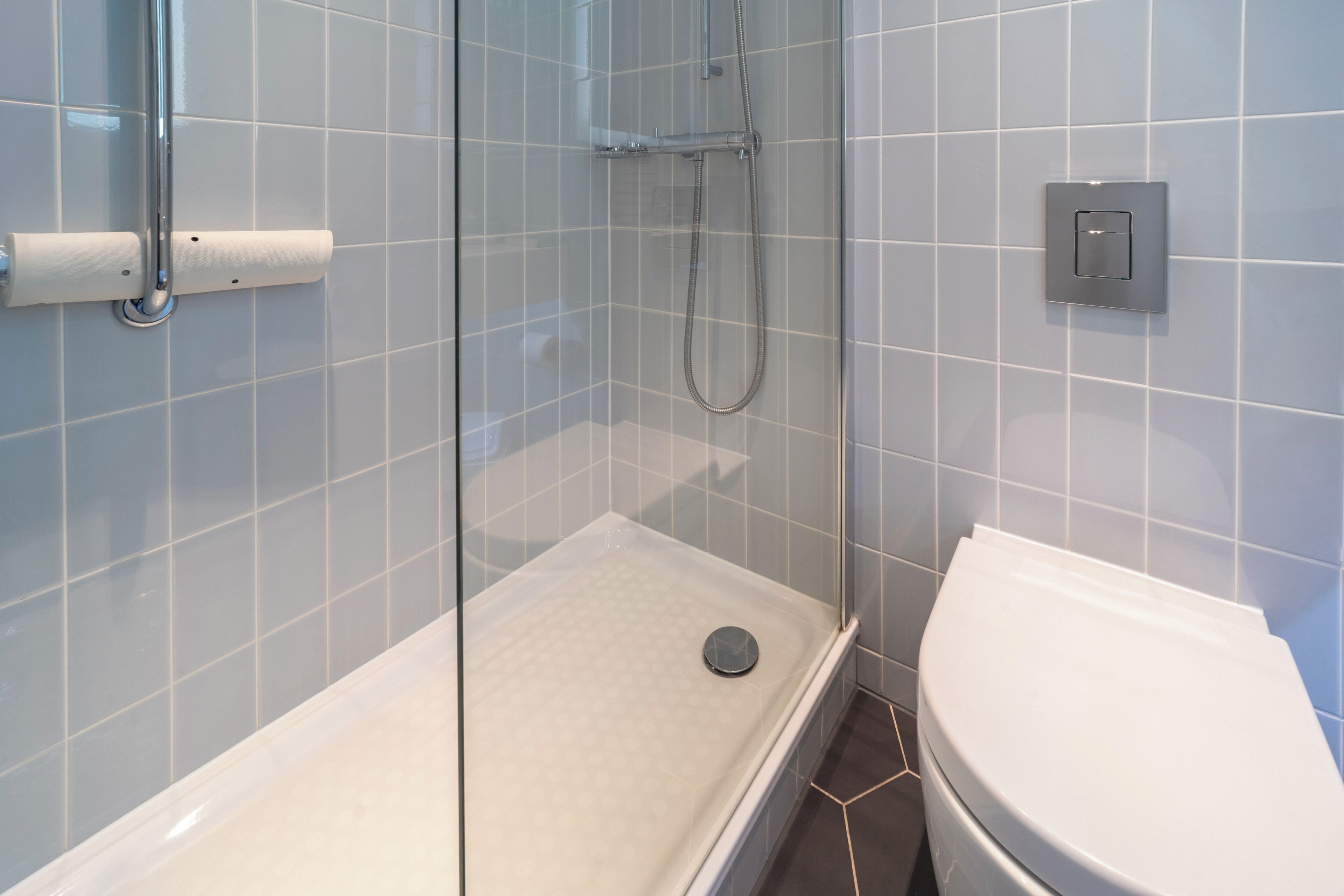 Ducha con puerta de vidrio, inodoro y panel de control en la pared.