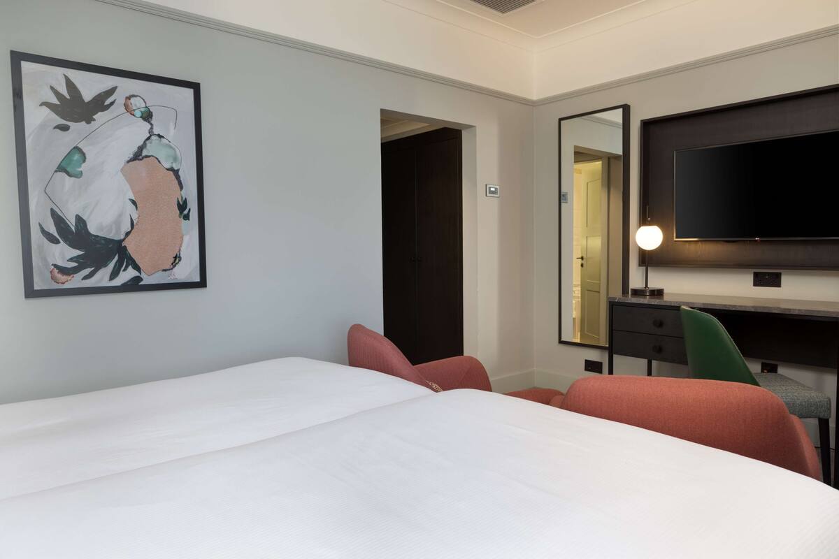 A hotel room with a large bed, a desk with a chair, a flat-screen TV, and a framed abstract painting on the wall.