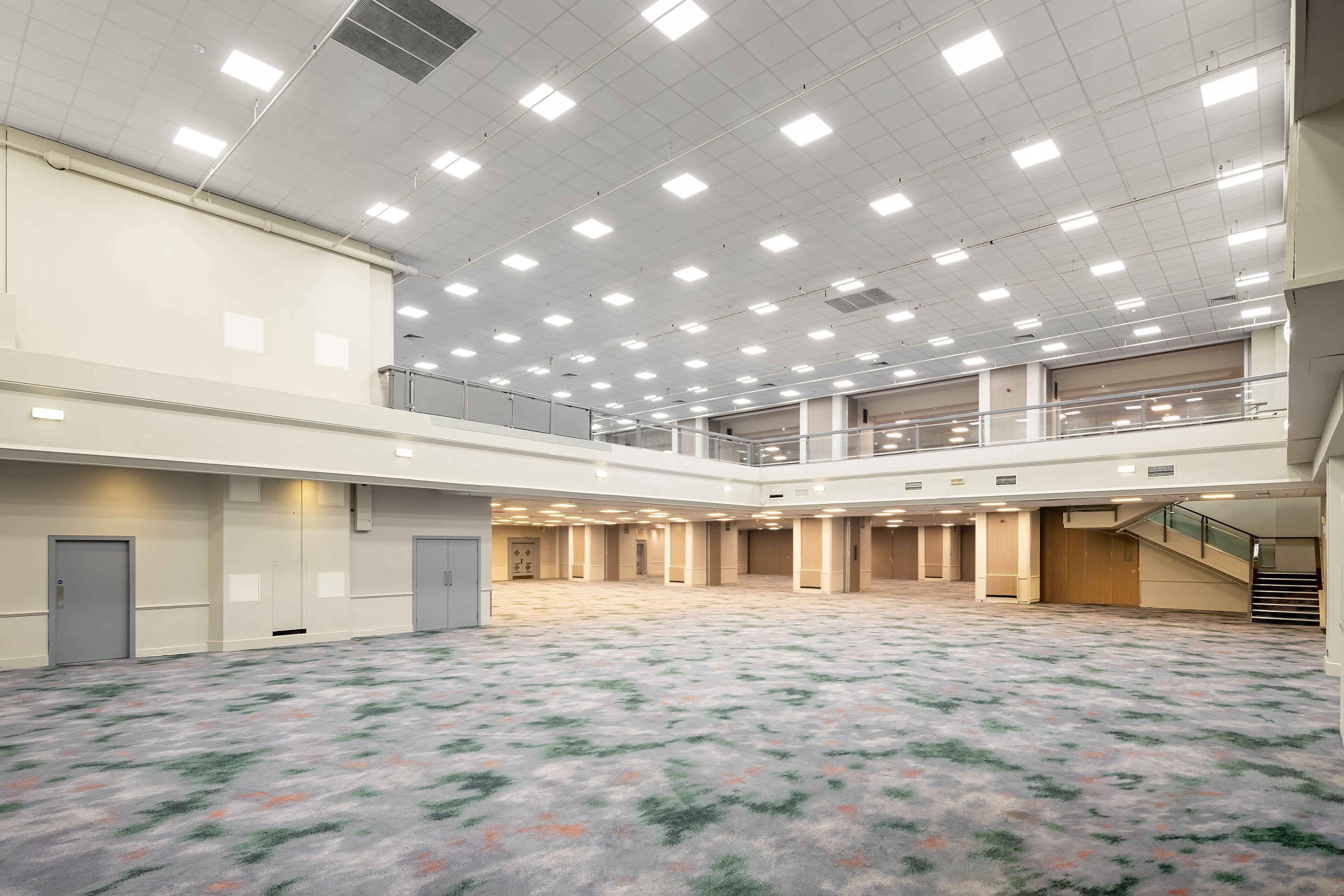 A spacious indoor area with a high ceiling, multiple doors, and a carpeted floor.