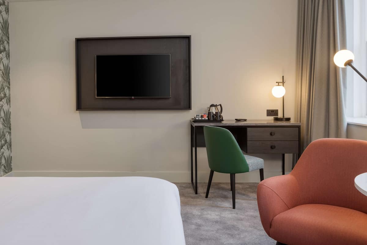 A hotel room with a bed, a desk with a chair, a television, and a lamp.