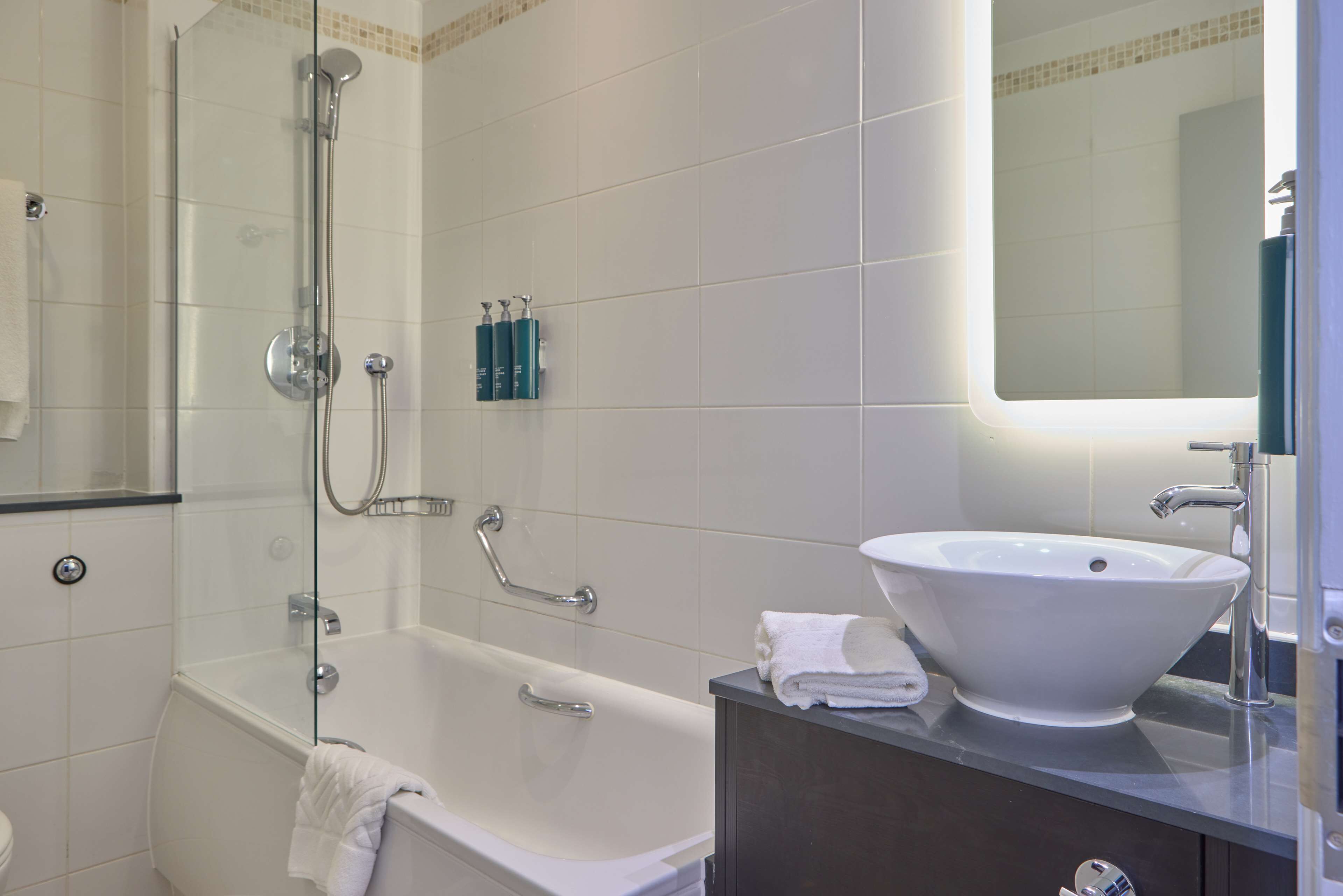 Een moderne badkamer met een glazen douchecabine, een wit bad en een wastafel met spiegel erboven.