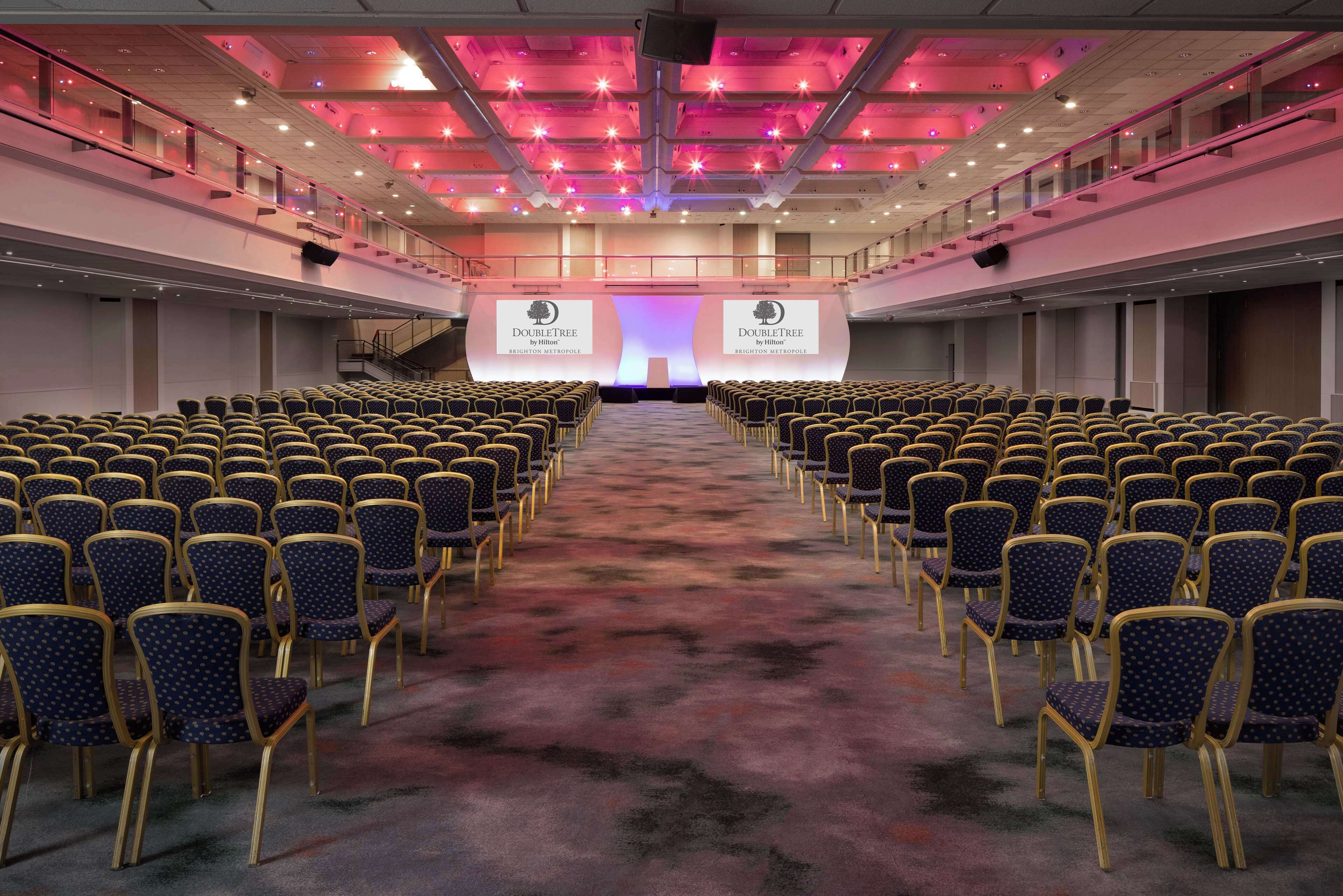 A large conference room with rows of chairs facing a stage with a presentation screen.