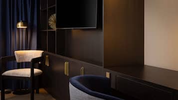 Una habitación moderna con un armario de madera oscura, un televisor de pantalla plana en la pared, un sillón tapizado en azul oscuro y una lámpara de pie.