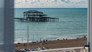 A coastal view with a pier extending into the sea, a beach with people and umbrellas, and a clear sky with clouds. - DoubleTree by Hilton Brighton Metropole (Brighton)