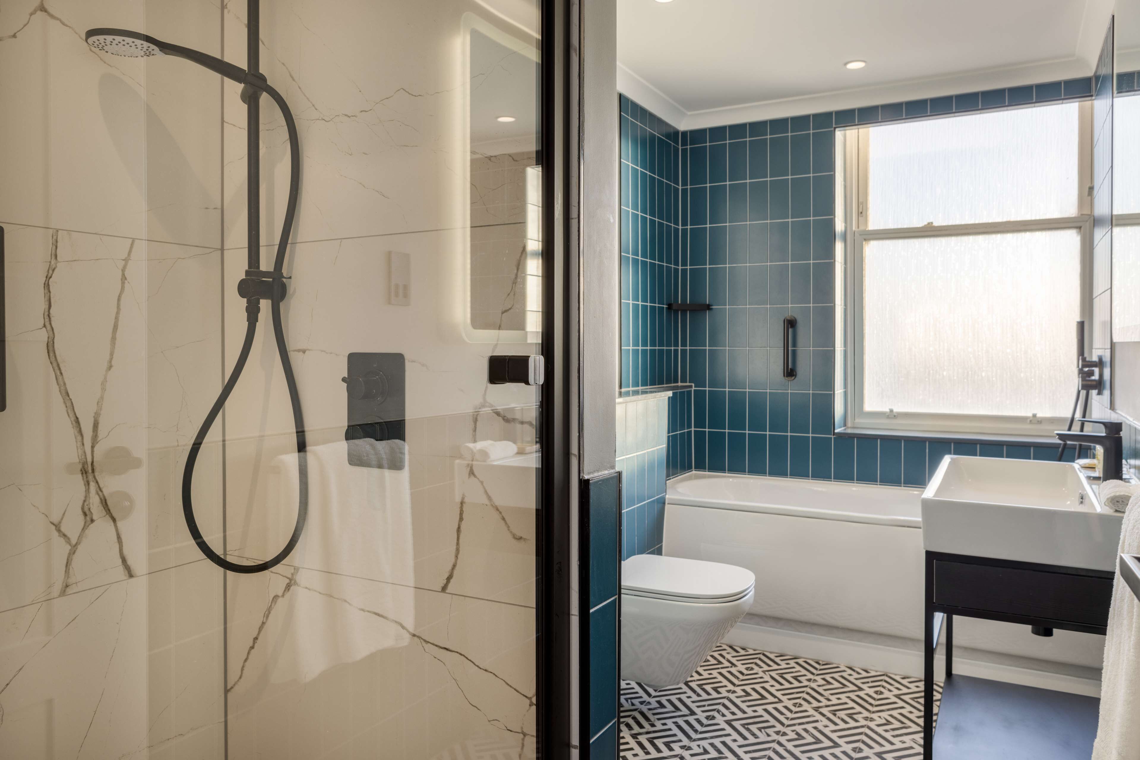 A bathroom with a shower, toilet, and sink, featuring marble walls and blue tiles.