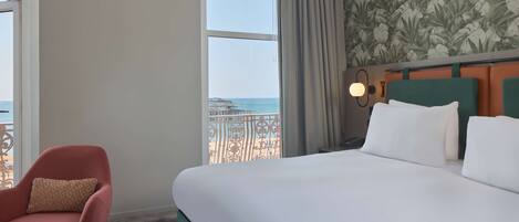 A hotel room with a large bed, a chair, a view of the beach, and a curtain.