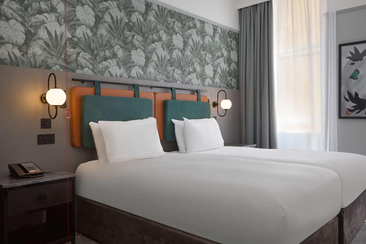 A hotel room with a large bed, two nightstands, a telephone, and a floral wallpaper.