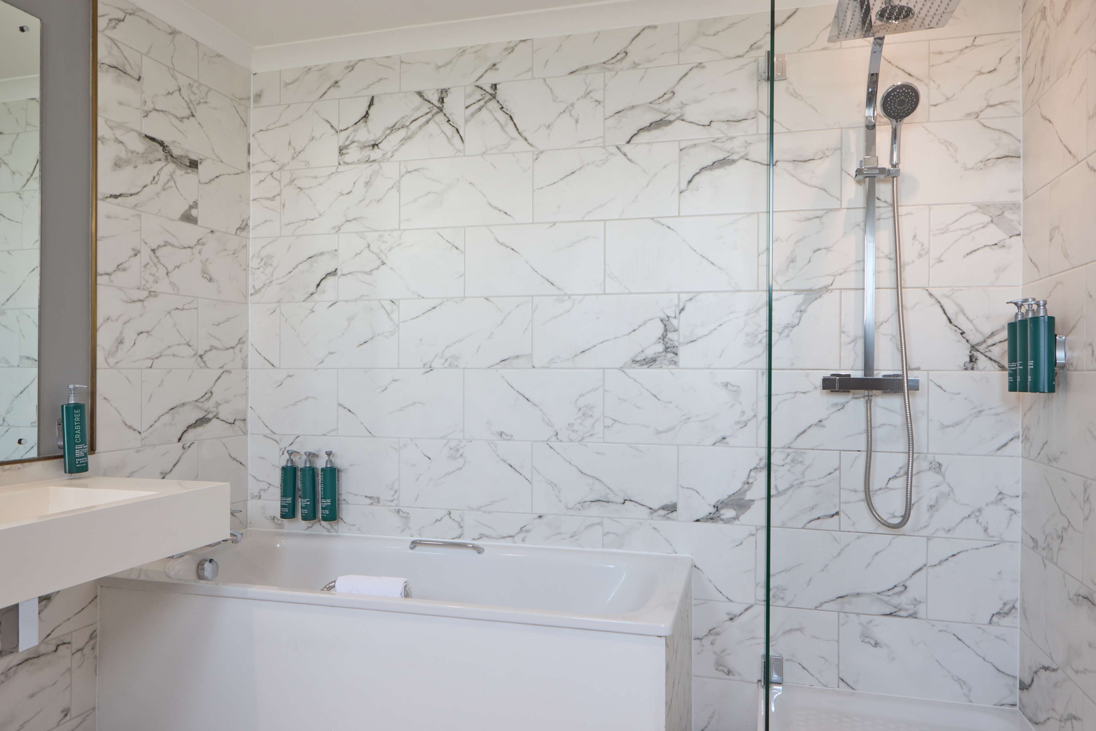 A modern bathroom with a marble wall, a glass-enclosed shower, and a white bathtub.