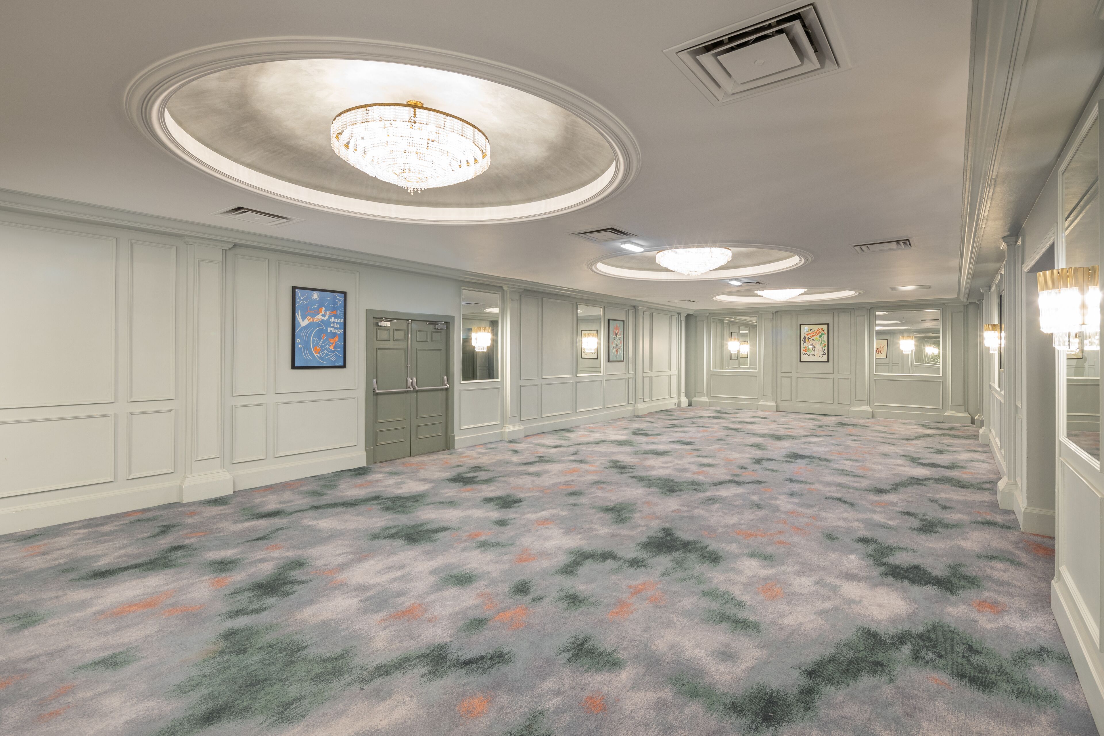 A spacious hotel lobby with a patterned carpet, recessed lighting, and a chandelier.