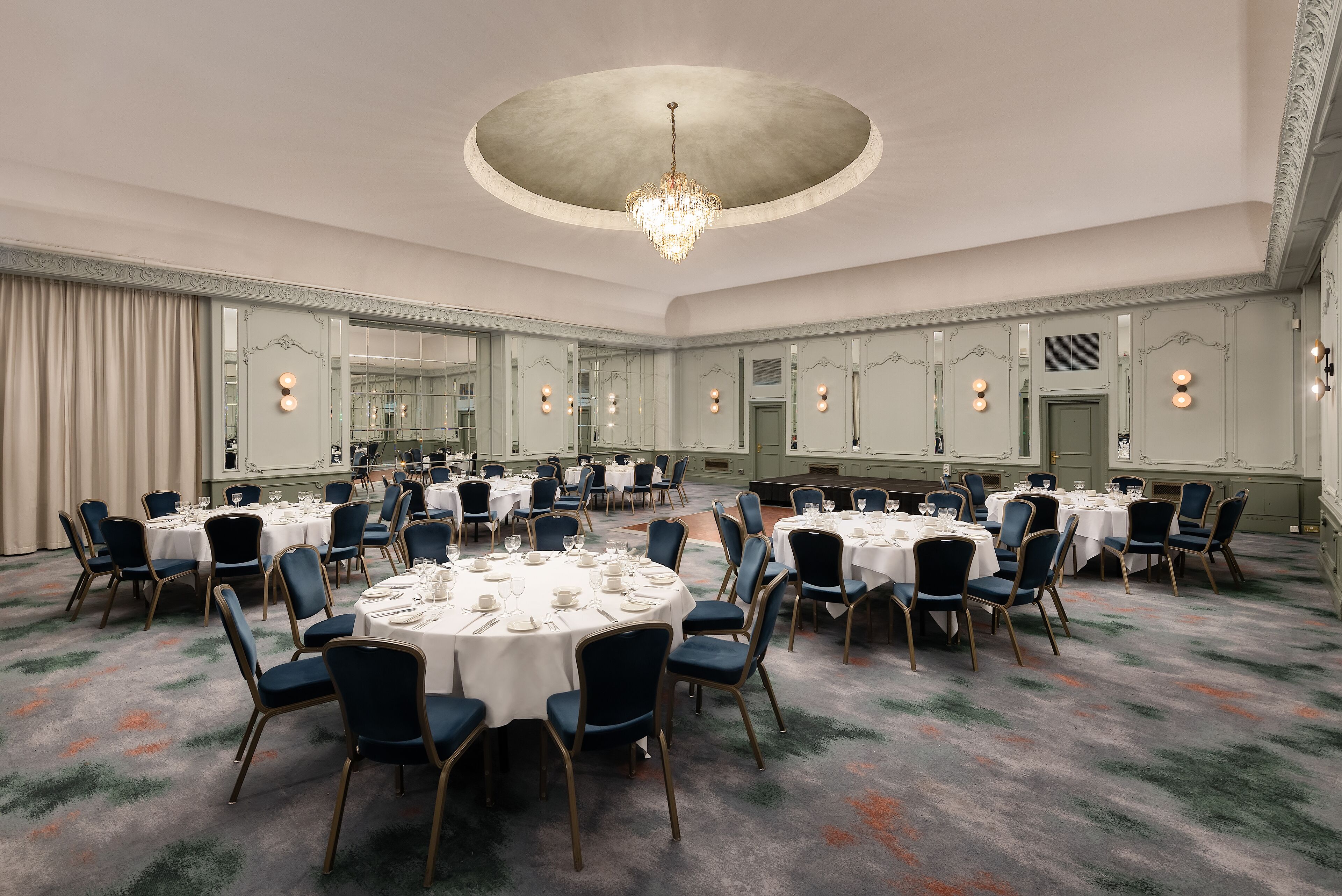 Une vaste salle de banquet avec des tables rondes et des chaises, un lustre et des murs recouverts de miroirs.