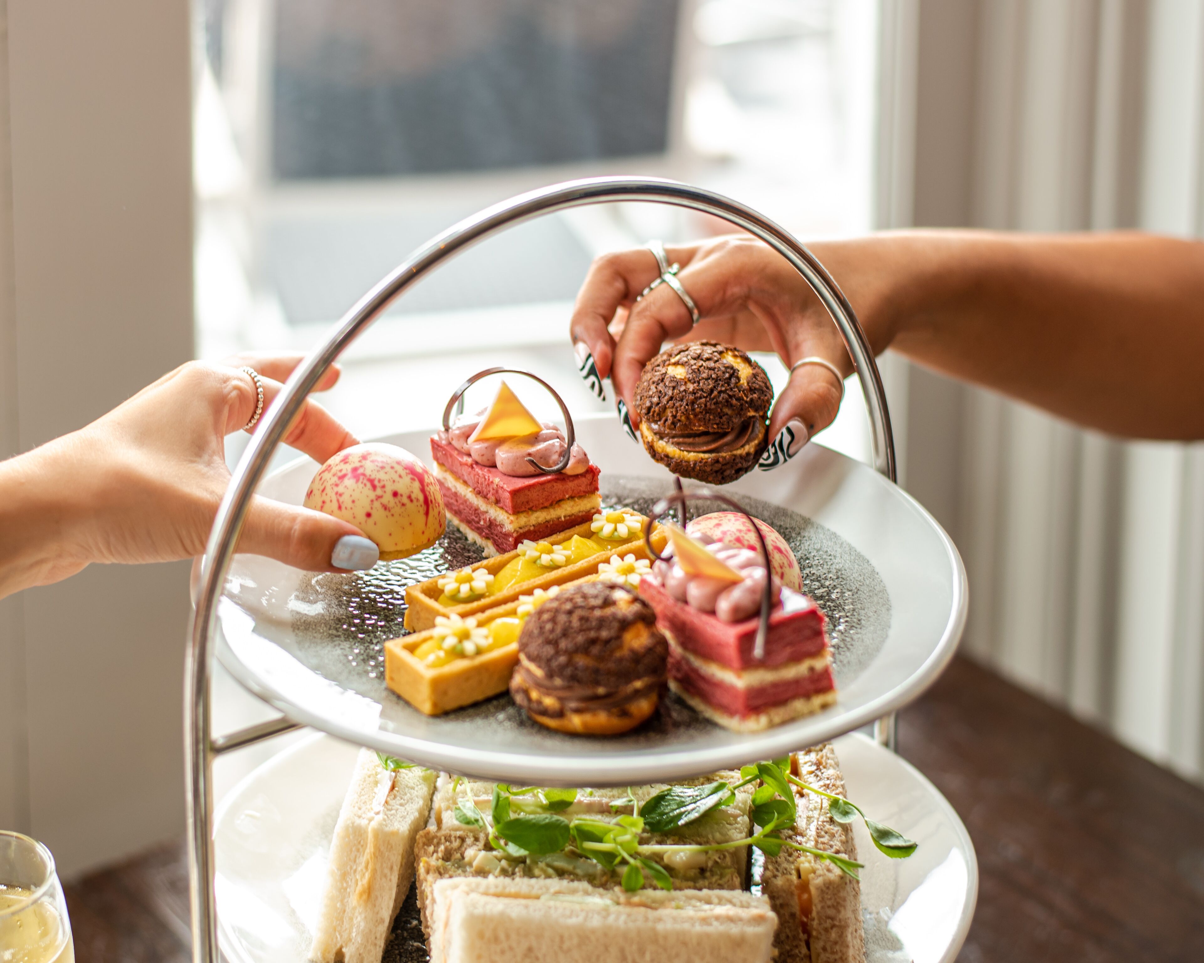 A tiered dessert stand with various pastries and sandwiches.