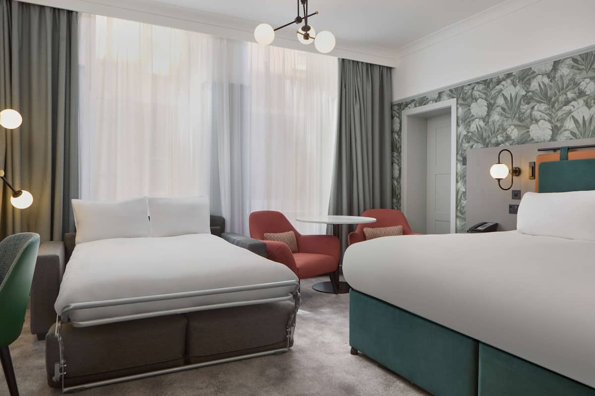 A hotel room with two beds, a small table, a chair, and a desk with a telephone.