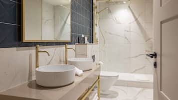 Un baño moderno con dos lavamanos redondos, un inodoro y una ducha a ras de suelo.